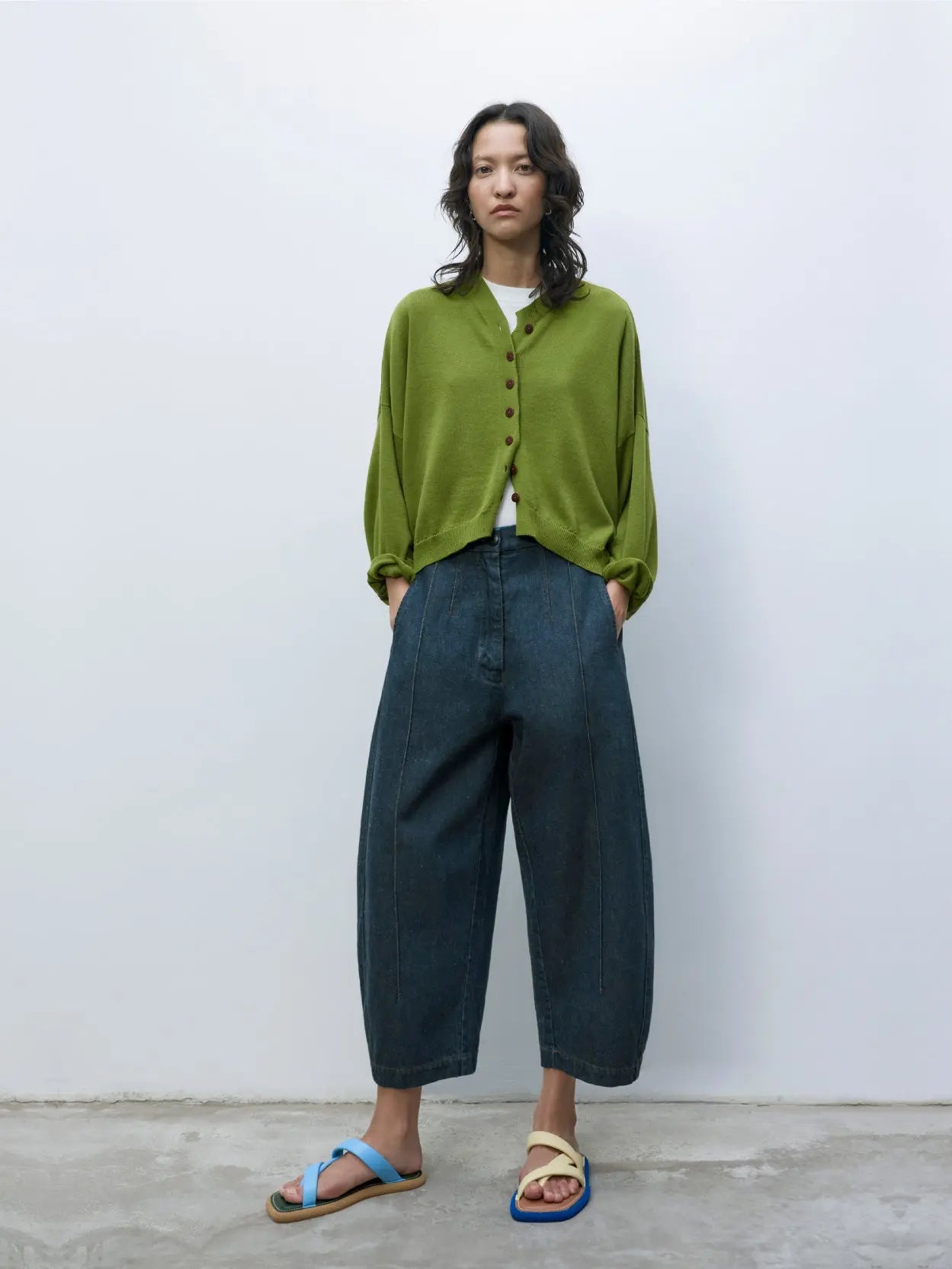 A green cropped cardigan with a V-neckline and brown buttons down the front is featured. The sleeves are long, and the fabric appears to be knit. The Cotton & Cashmere Cardigan Woodbine by cordera, available at Bassalstore Barcelona, has a label at the inner neckline. The background is white.