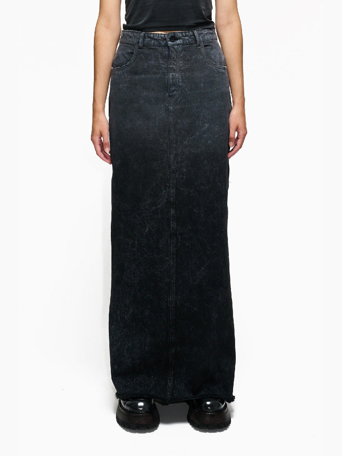 The Annul Skirt Faded Away Grey by Hope is a high-waisted, ankle-length denim skirt in a faded black wash. This long skirt features side pockets, belt loops, and a front zipper with a button closure. The hem is slightly frayed, giving it a distressed look.