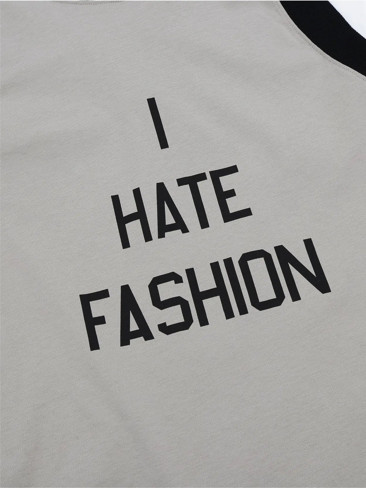 A long-sleeve shirt with a white body and sleeves, featuring a contrasting black neckline and armholes. It boasts a bold "I HATE FASHION" print on the beige front panel. Discover this edgy I Hate Fashion T-Shirt Re-Edition by Sunnei at BassalStore, your go-to fashion destination in Barcelona.