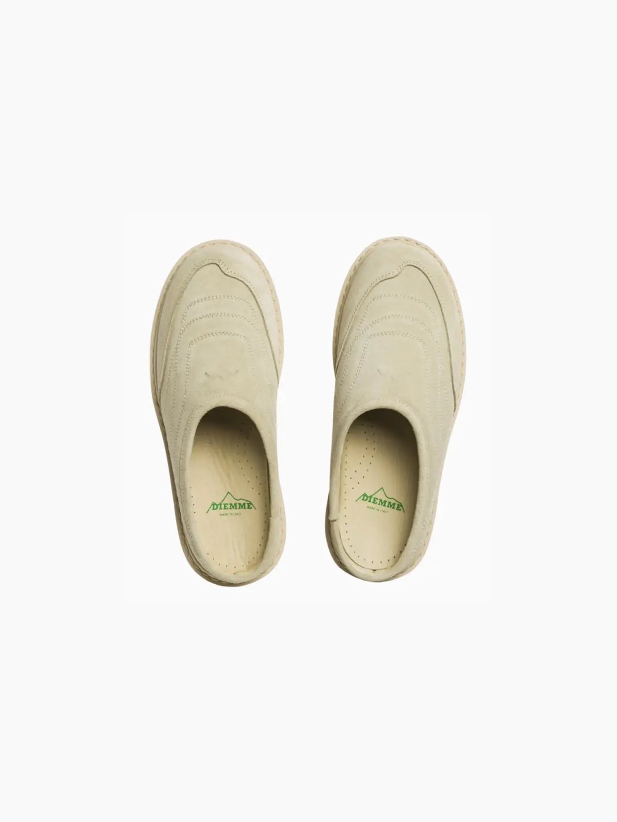 A single beige slip-on shoe, the "Maggiore Ecru Suede" by Diemme, available at bassalstore in Barcelona, featuring a rugged, lugged sole and minimalistic design. The upper part showcases subtle stitched detailing for texture. The shoe has a closed toe and an open back, resembling a mule style. The outsole is slightly thicker, offering added traction.