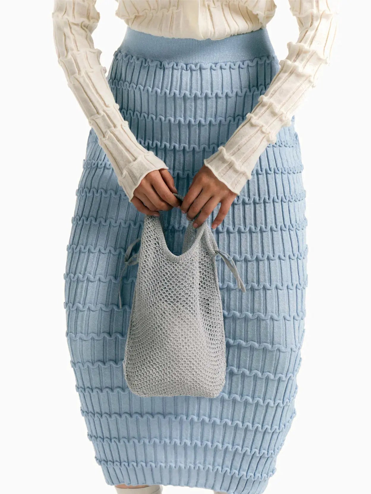 A Rus Mizuki Skirt Light Blue, knitted with a ribbed, wavy texture pattern from Bassalstore. The form-fitting skirt features an elastic waistband for a snug fit and boasts a knee-length design, displayed beautifully on a plain white background. Perfect for your next visit to Barcelona!