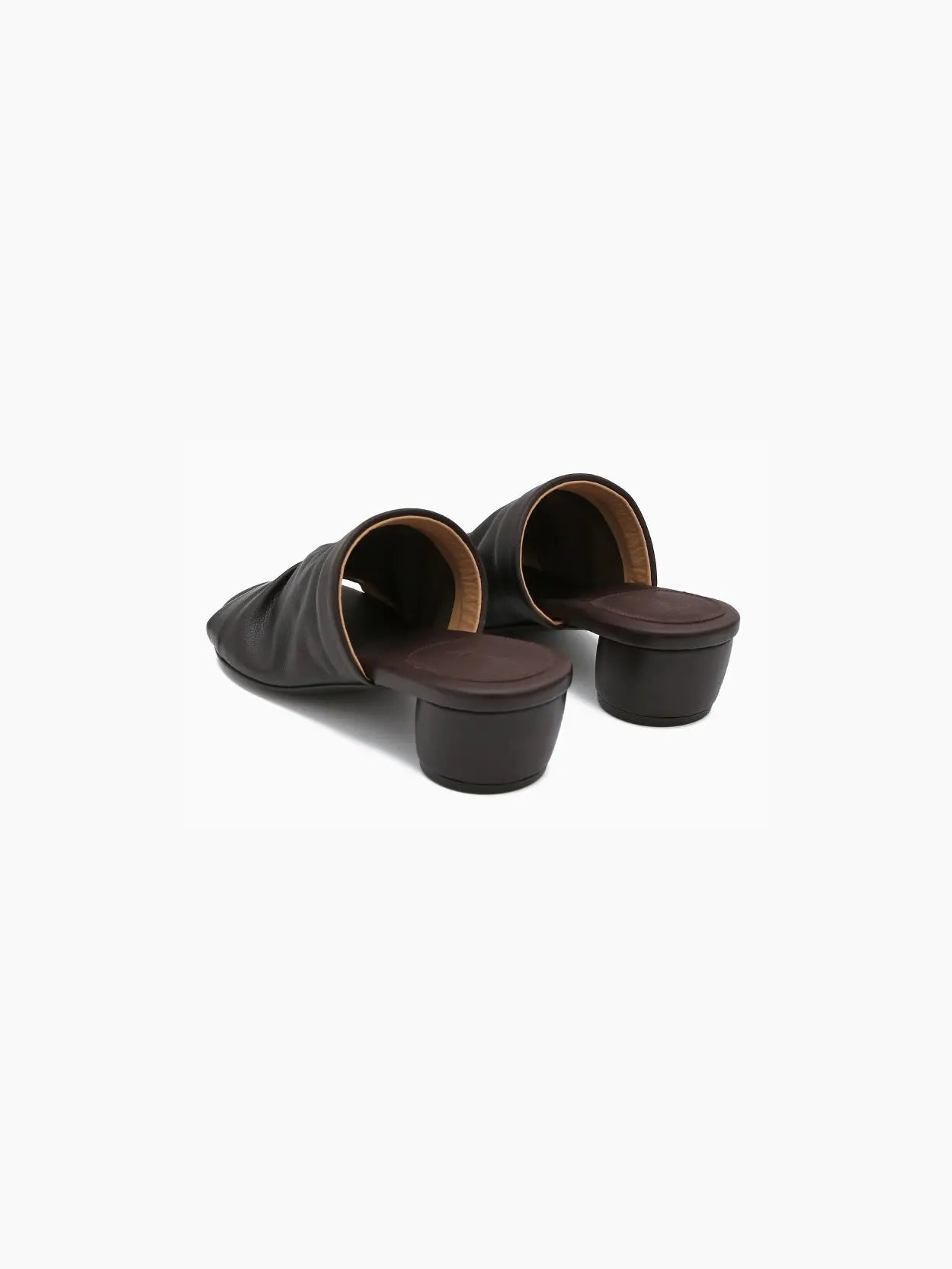 A dark brown mule-style sandal with a wide strap covering the upper foot and an open toe, available at Bassalstore. The Otto Sandal Dark Brown features a low, chunky heel and a minimalist design. Pictured against a white background in a side view, this shoe embodies chic Barcelona fashion from Marsèll.
