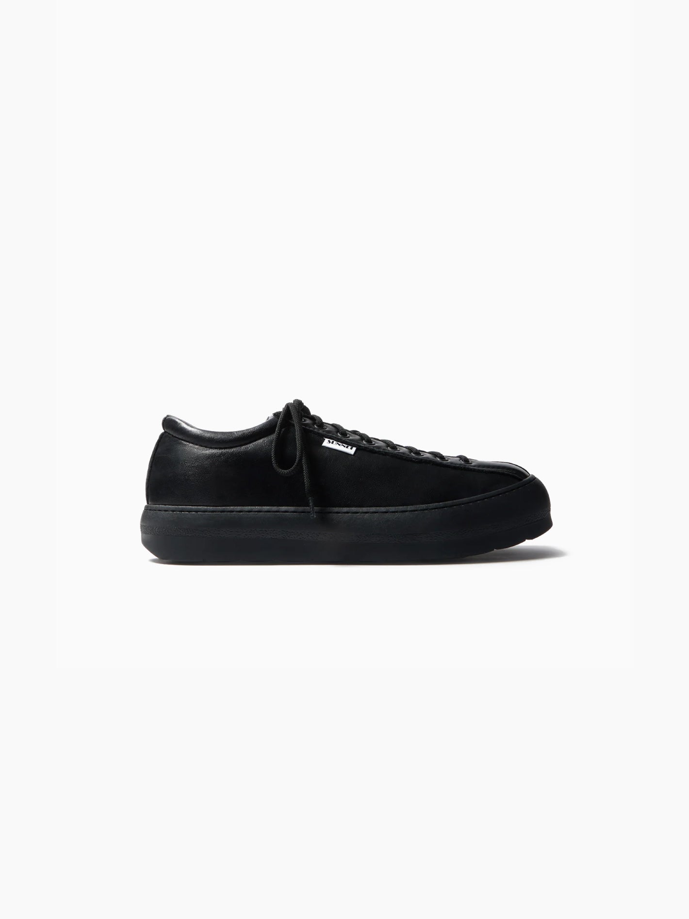 A side view of a single "Dreamy Bowling Black Shoe" by Sunnei on a white background. The sneaker features a low-top design with a smooth, minimalistic appearance, black laces, and a thick black sole. Made in Italy, the lace-up shoe appears to be made of a soft, suede-like material.