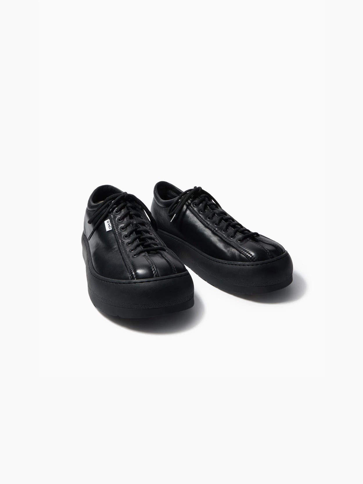 A side view of a single "Dreamy Bowling Black Shoe" by Sunnei on a white background. The sneaker features a low-top design with a smooth, minimalistic appearance, black laces, and a thick black sole. Made in Italy, the lace-up shoe appears to be made of a soft, suede-like material.