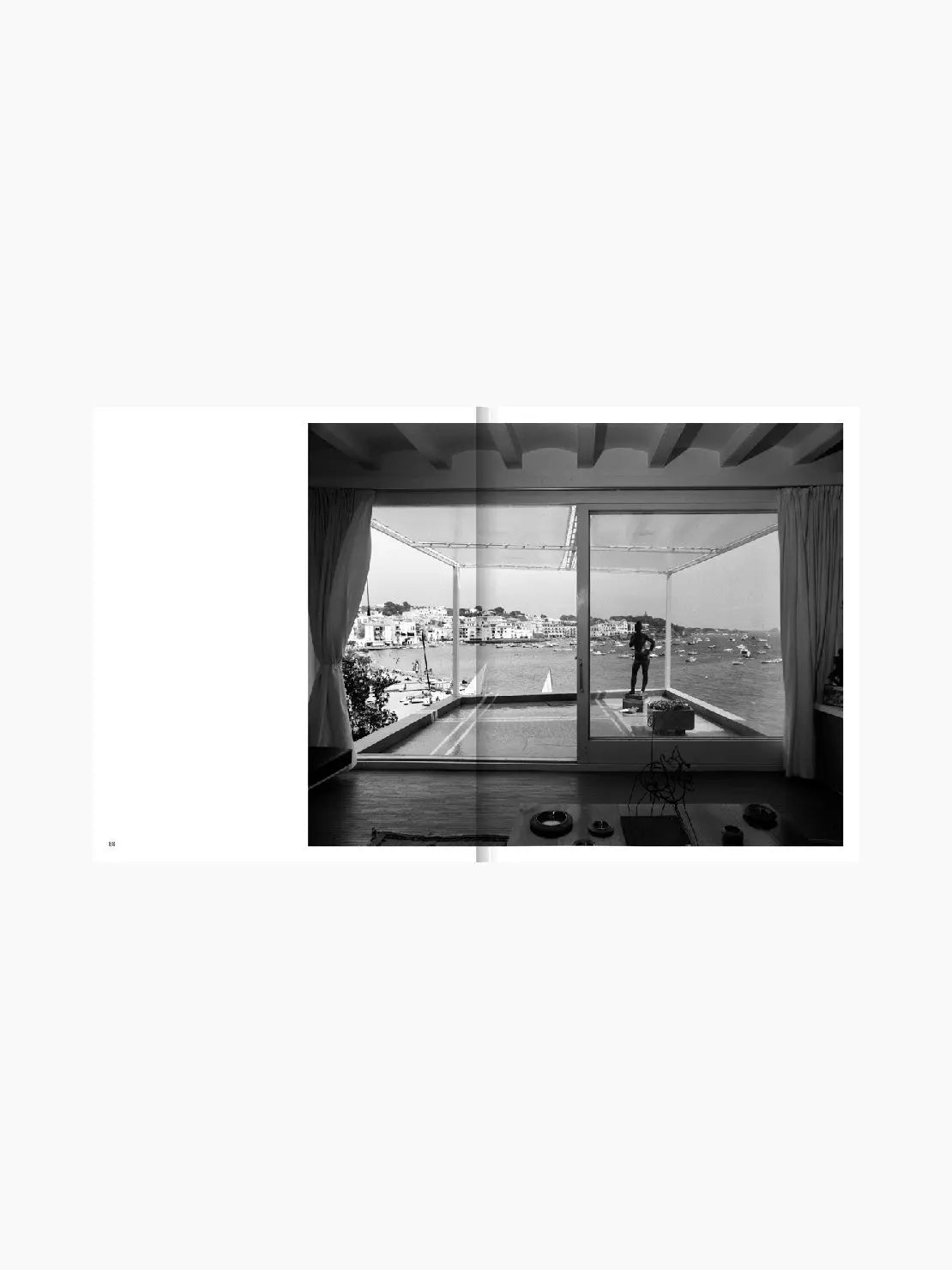 A book cover titled "The Modern Architecture of Cadaqués: 1955–71." The cover features a black and white photograph of a modern, minimalist living space with large windows. Published by Apartamento and available at Bassalstore, this edition resonates with the architectural elegance of nearby Barcelona.