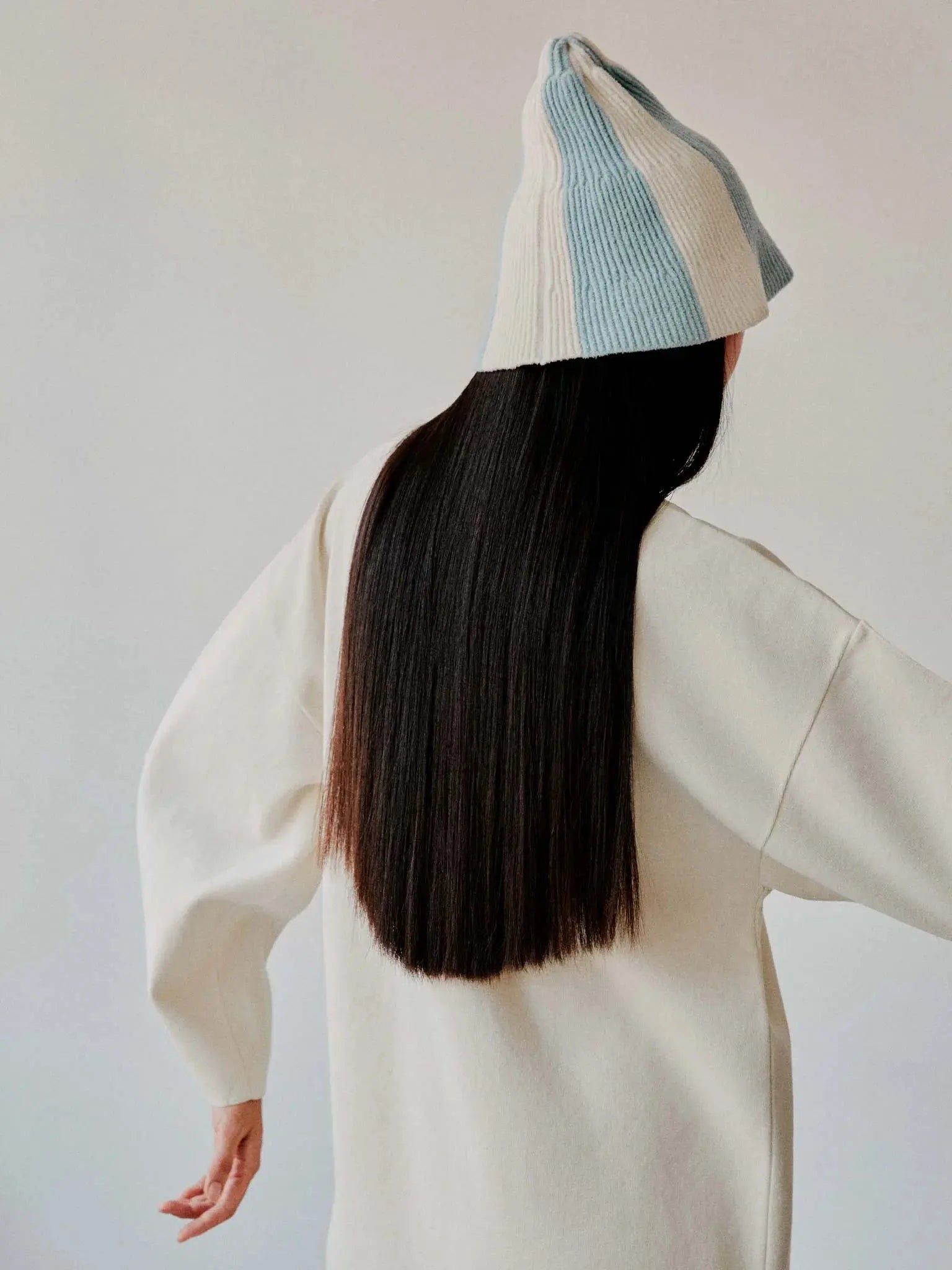 A conical knitted hat with alternating blue and white vertical stripes, available at Bassalstore. The Yuzu Hat by Rus features a ribbed texture of the fabric that is clearly visible, and the hat has a slightly flared brim at the bottom. The background is plain white.