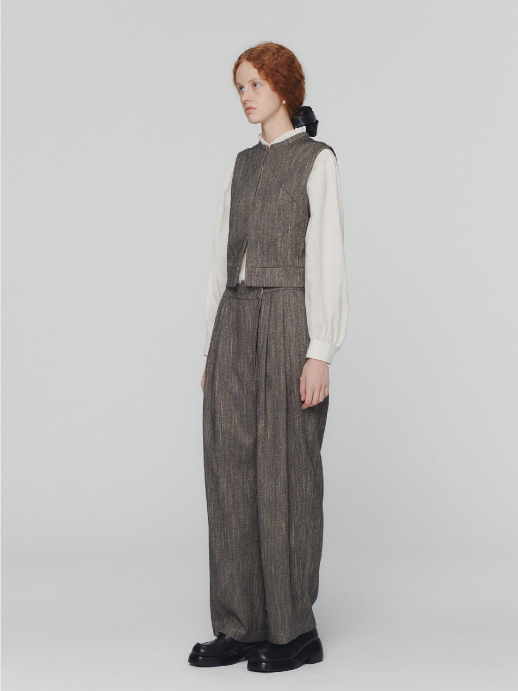 Amomento's Wool Tweed Wrap Pants in Charcoal feature a high-waisted wide-leg silhouette with a subtle herringbone pattern. These pants come with front pleats and practical pockets, crafted from wool-like fabric for a tailored and slightly textured appearance. With their simple, classic design, these pants offer a polished look.