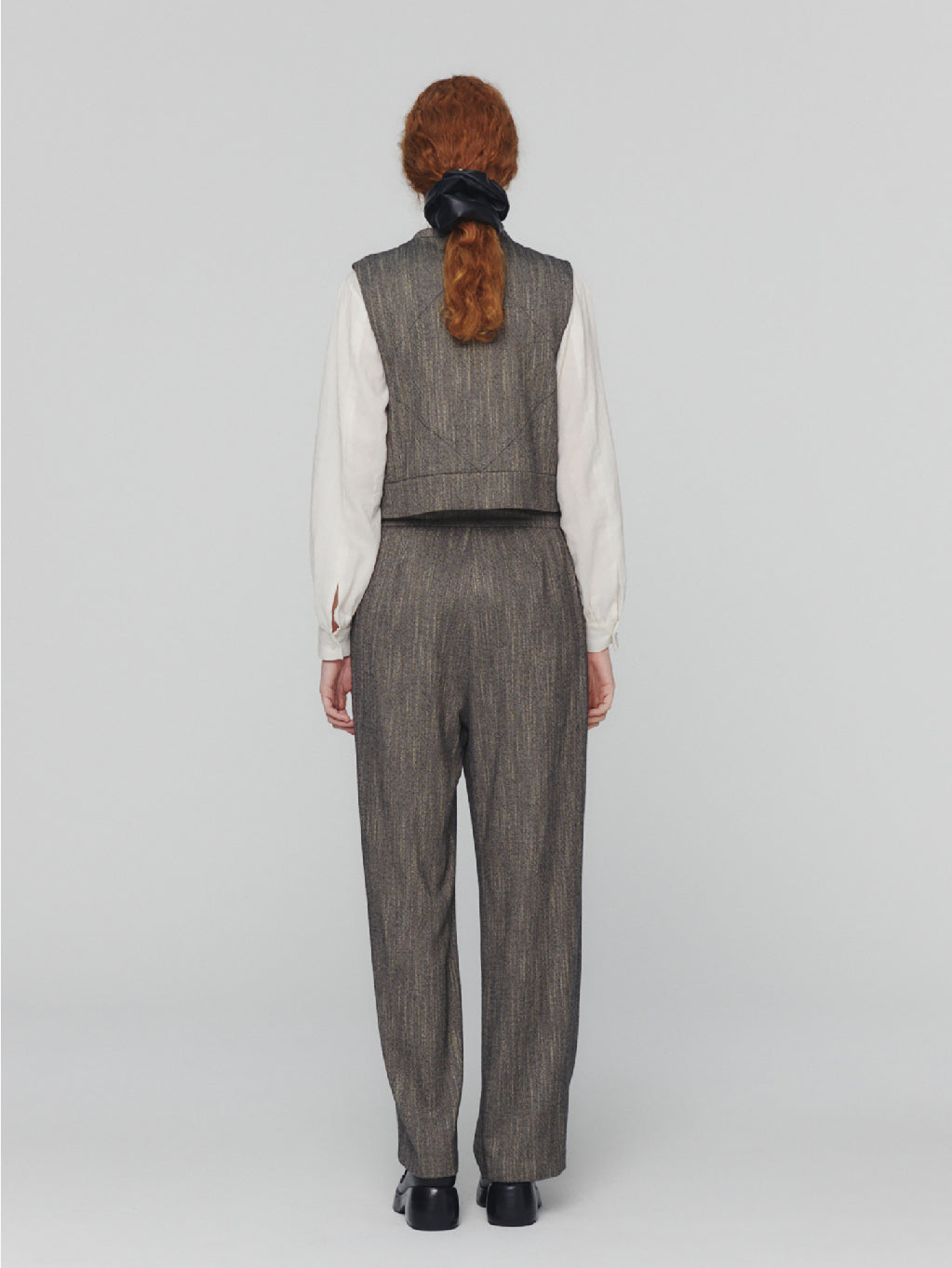 Amomento's Wool Tweed Wrap Pants in Charcoal feature a high-waisted wide-leg silhouette with a subtle herringbone pattern. These pants come with front pleats and practical pockets, crafted from wool-like fabric for a tailored and slightly textured appearance. With their simple, classic design, these pants offer a polished look.