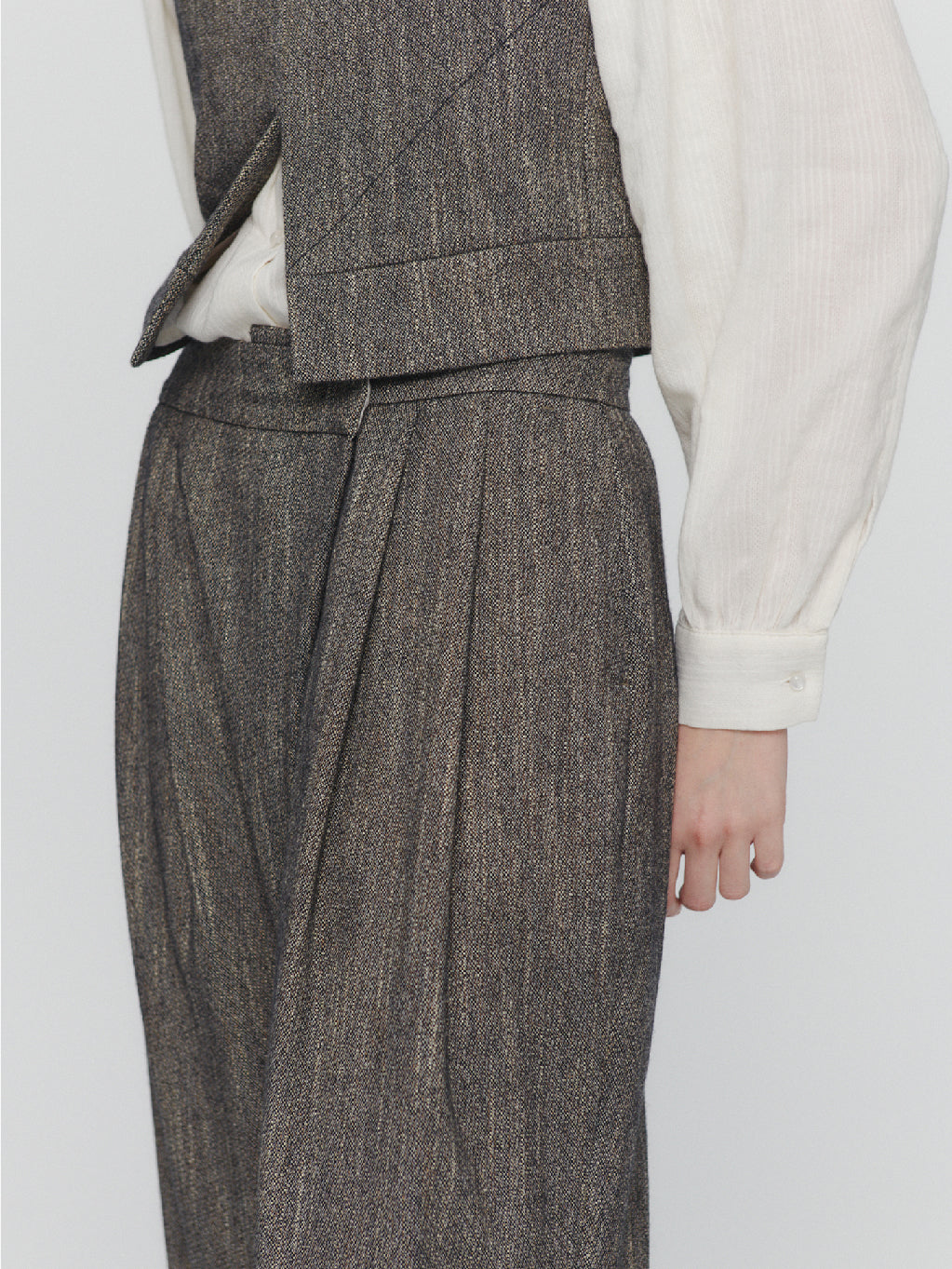 Amomento's Wool Tweed Wrap Pants in Charcoal feature a high-waisted wide-leg silhouette with a subtle herringbone pattern. These pants come with front pleats and practical pockets, crafted from wool-like fabric for a tailored and slightly textured appearance. With their simple, classic design, these pants offer a polished look.