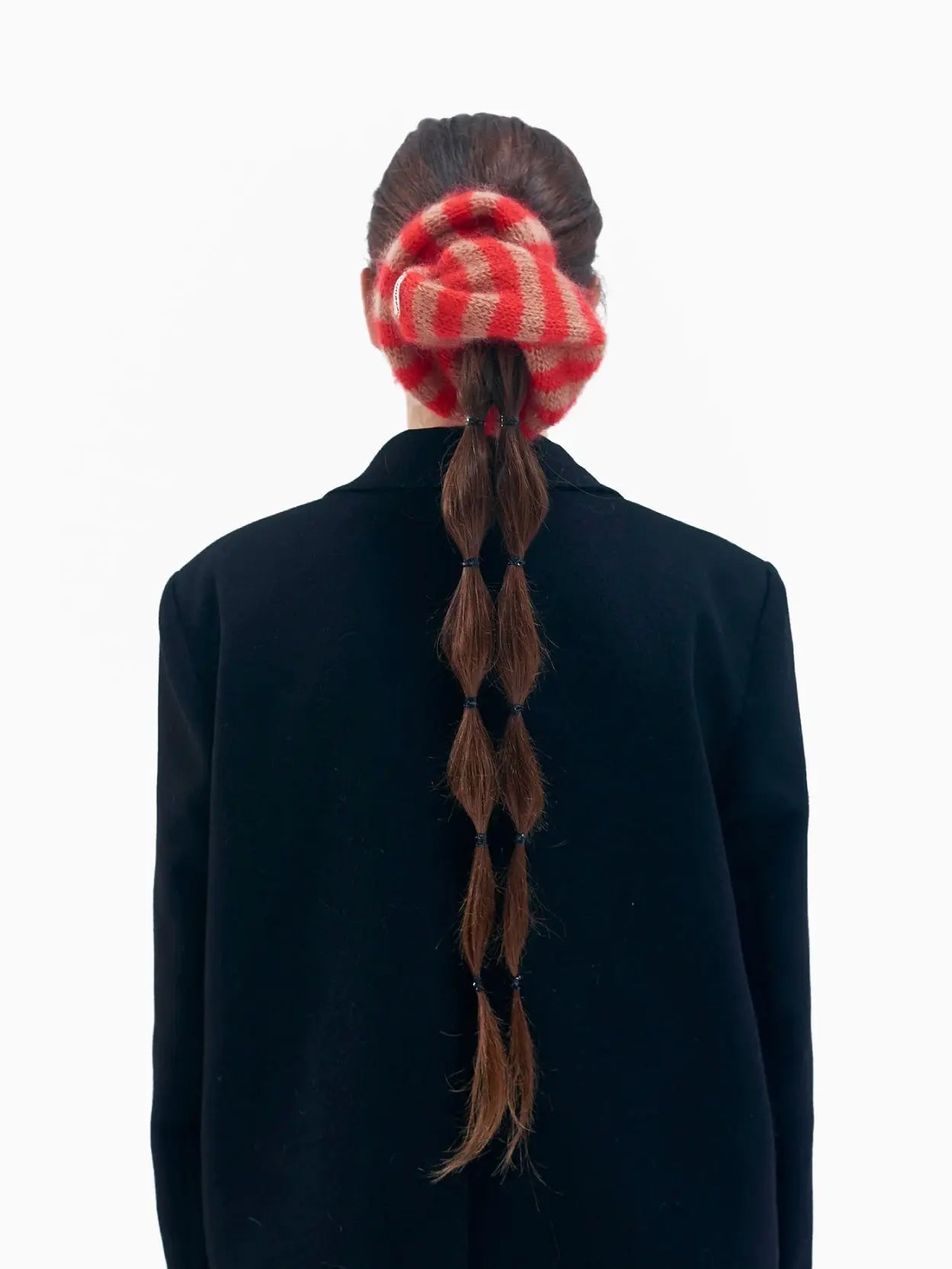 A round, knitted scrunchie with red and beige stripes is displayed against a plain white background. There is a small white tag with red and black writing attached to it. Shop the stylish Amapola Mohair Scrunchie by Tomasa at Bassalstore, your go-to store in Barcelona for unique finds.