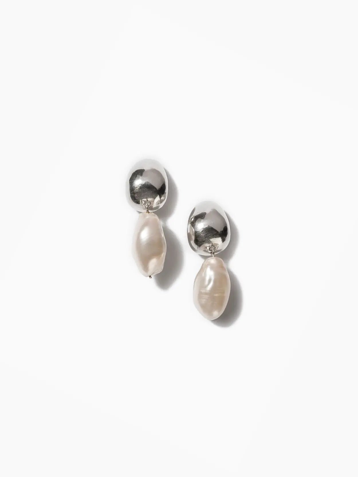 A pair of elegant Ava Earrings with small, silver spherical studs and irregular, baroque freshwater pearls dangling from each, available exclusively at Nathalie Schreckenberg Bassalstore, set against a plain white background.