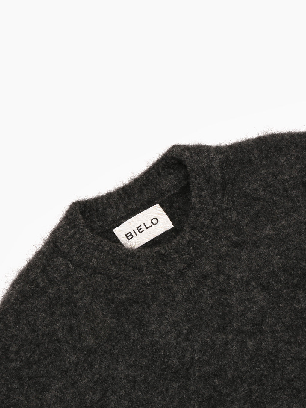 The Mael Sweater Grey by Bielo, featuring a dark gray color with long sleeves and a round collar, is crafted from extrafine merino wool and has a fuzzy texture. It's laid flat on a white background with the tag inside the collar reading "BRIXO.