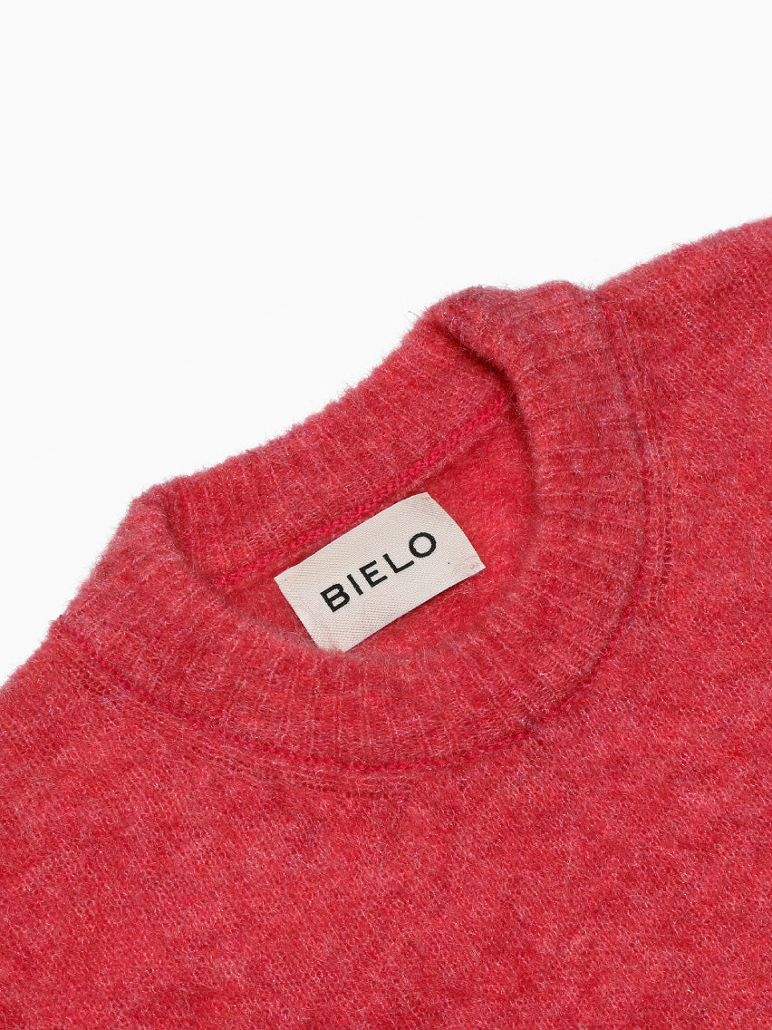 The Mael Sweater Pink by Bielo is a soft, round-collar sweater made from extrafine merino wool, featuring long sleeves and showcased against a plain white background.