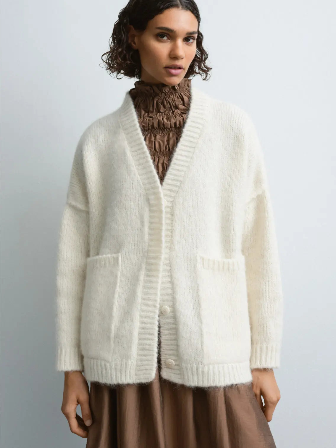 A cream-colored, long-sleeve Baby Alpaca Cardigan Natural displayed on a white background. It features a deep V-neck, front button closure, ribbed cuffs, two front pockets, and a relaxed fit. The label "Cordera" is visible on the inside neckline. Available exclusively at Bassalstore in Barcelona.