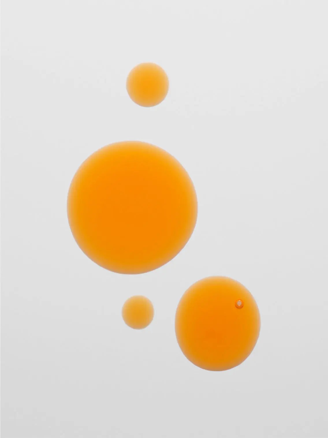 Four orange bubbles of varying sizes with smooth edges are suspended against a neutral white background. The bubbles, reminiscent of the dynamic energy found in a bustling Barcelona store, are arranged in a staggered formation, with the largest bubble near the center and two smaller bubbles directly above and below it. These vibrant orbs perfectly encapsulate the essence of Jorgobé's Bakuchiol Face Oil 30ml.