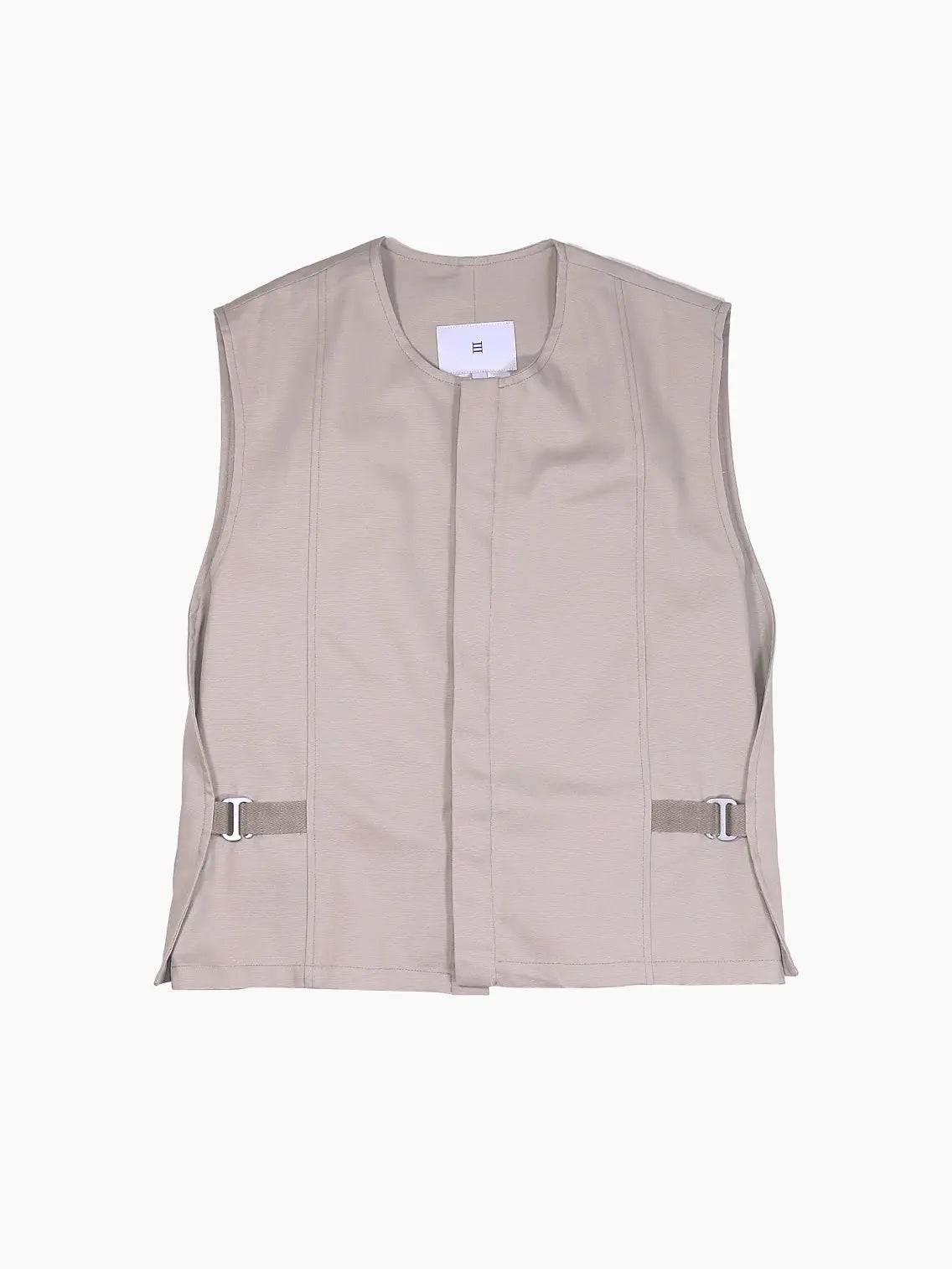 A sleeveless, light beige utility vest with minimalistic design, featuring side buckle adjustments and a front concealed closure. The lightweight fabric contributes to its plain, unembellished appearance. Available exclusively at Bassalstore in Barcelona. This is the Beige Vest by Bastida x Bassal Store.