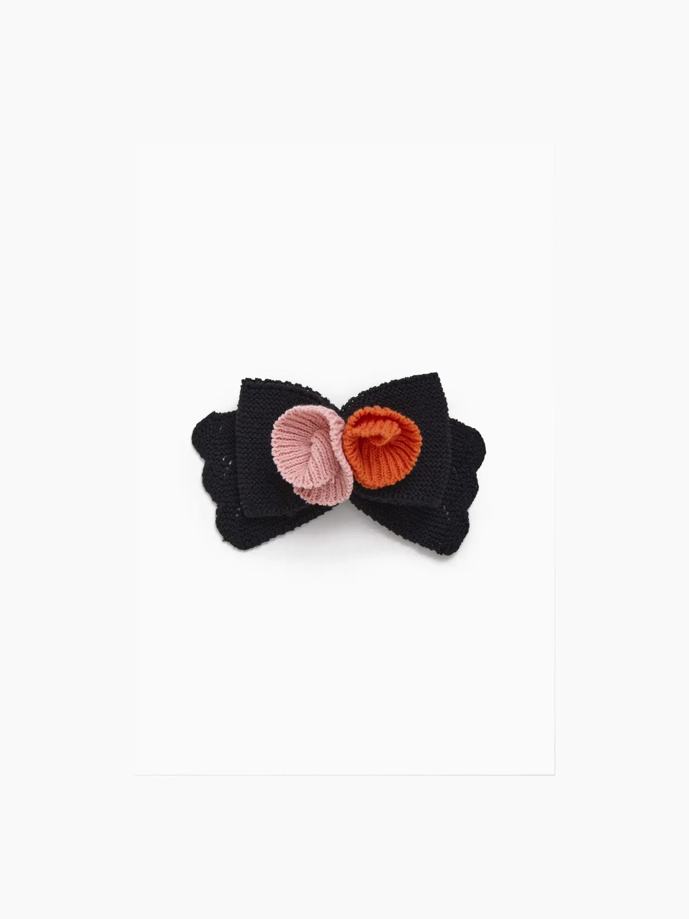 A Black Bow Hairclip with scalloped edges, adorned with two small circular embroidered flowers in pink and orange at the center, perfectly captures the charm of Barcelona. This lovely accessory from Tomasa is set against a plain white background.