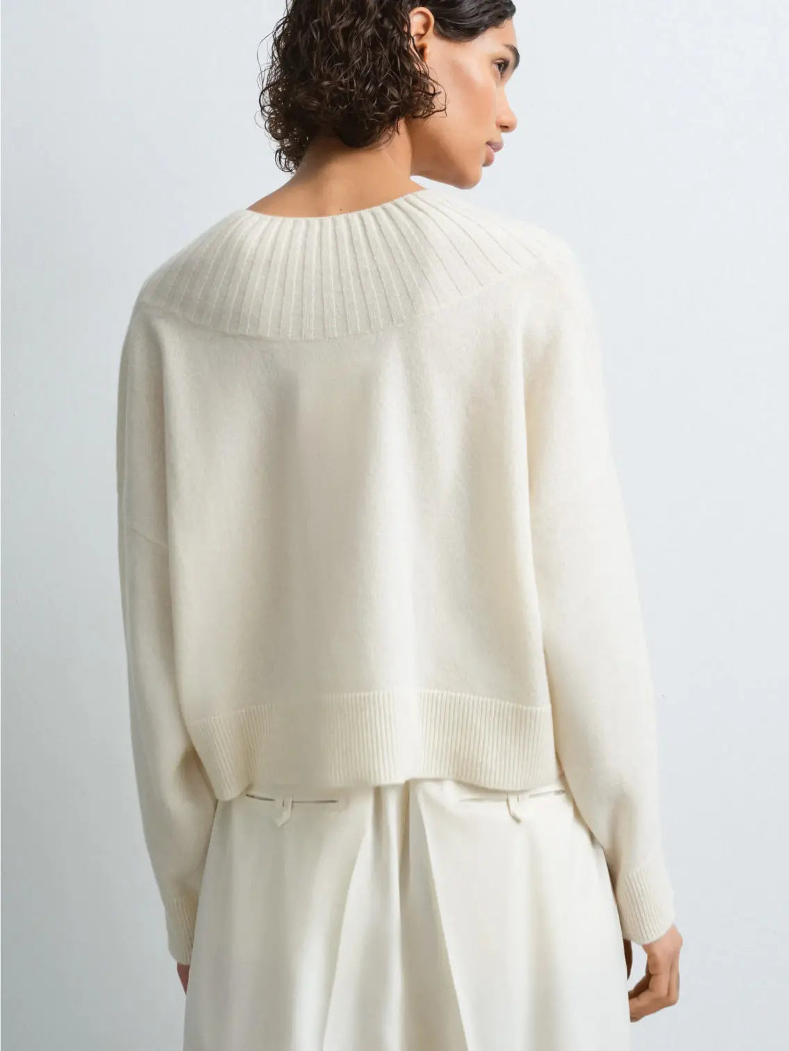 A cream-colored knit sweater with a V-neck collar and long sleeves. The Cashmere Ribbed Neck Sweater Natural by Cordera, available at Bassalstore, has a ribbed design on the neckline, cuffs, and hem, creating a cozy and slightly oversized look. It is laid out flat on a white background. Perfect for a stylish day in Barcelona.
