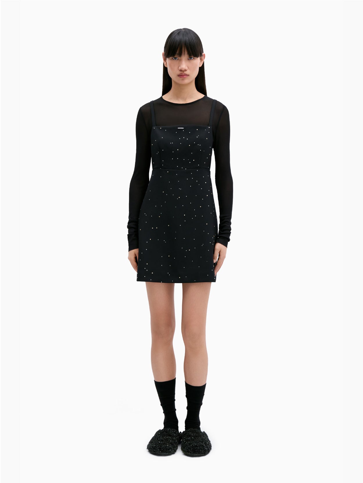 The Embellished Mini Dress Black by Cordera is a black sleeveless dress adorned with thin straps and small white star-like patterns scattered across the fabric. It features an open back, a square neckline, and an A-line silhouette.