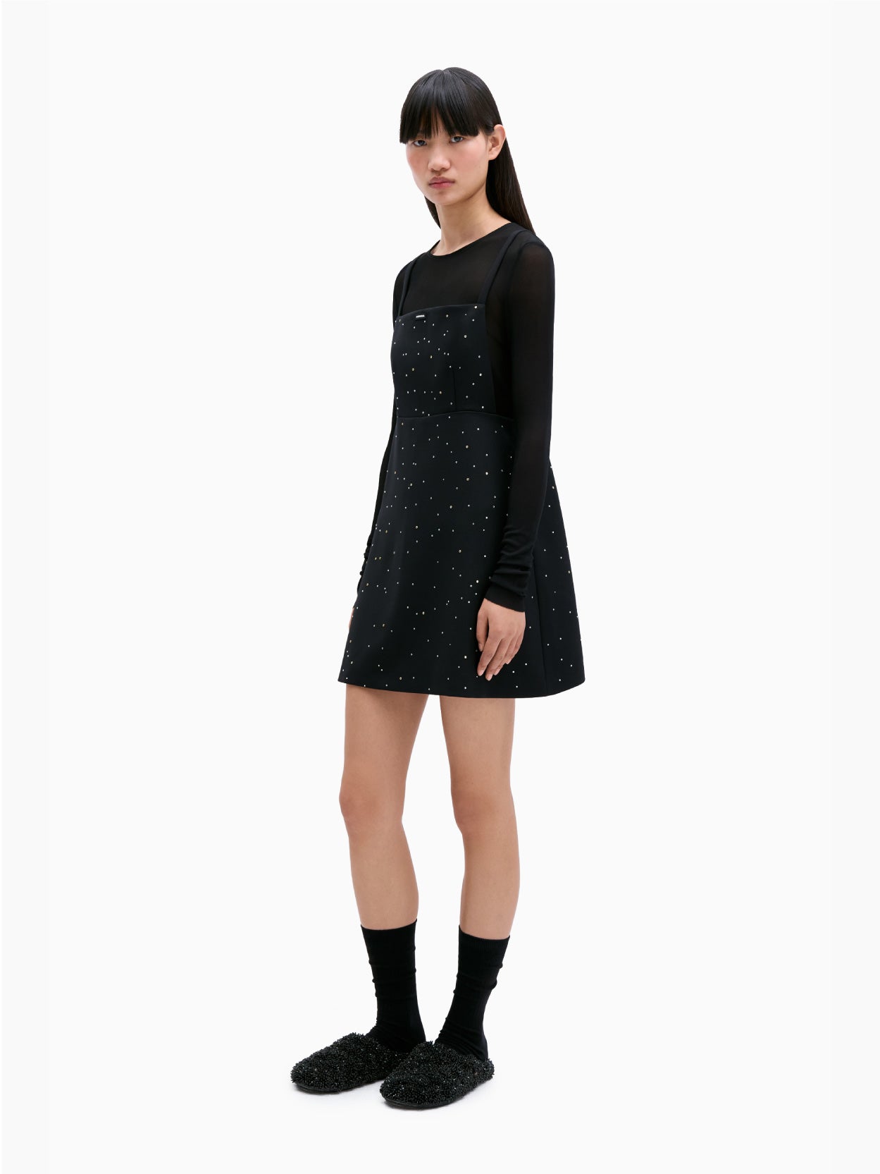 The Embellished Mini Dress Black by Cordera is a black sleeveless dress adorned with thin straps and small white star-like patterns scattered across the fabric. It features an open back, a square neckline, and an A-line silhouette.