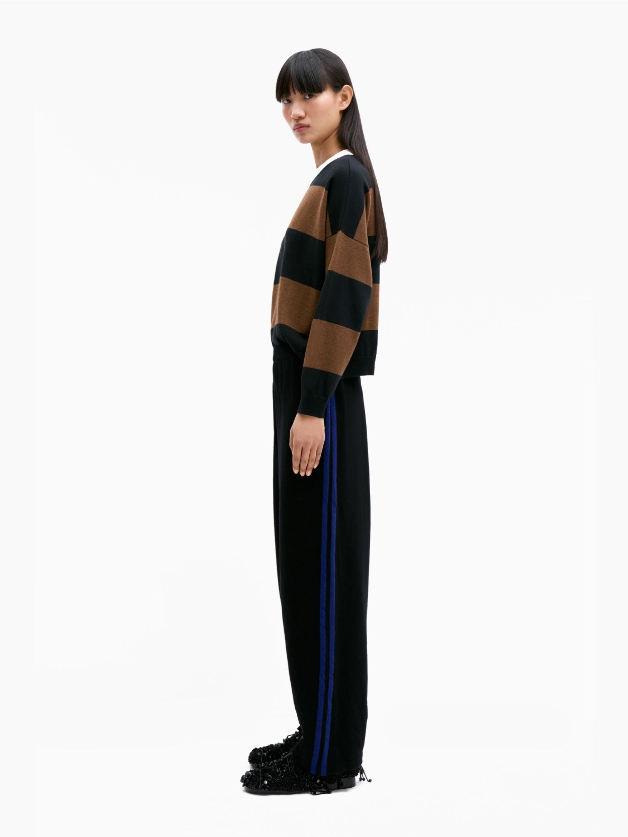 The Cordera Merino Wool Pants in black showcase a simple design with blue side stripes running down the length of each leg. Crafted from premium merino wool and featuring an elasticated waistband, these pants exhibit a relaxed sporty style. They are elegantly displayed on a flat white background.