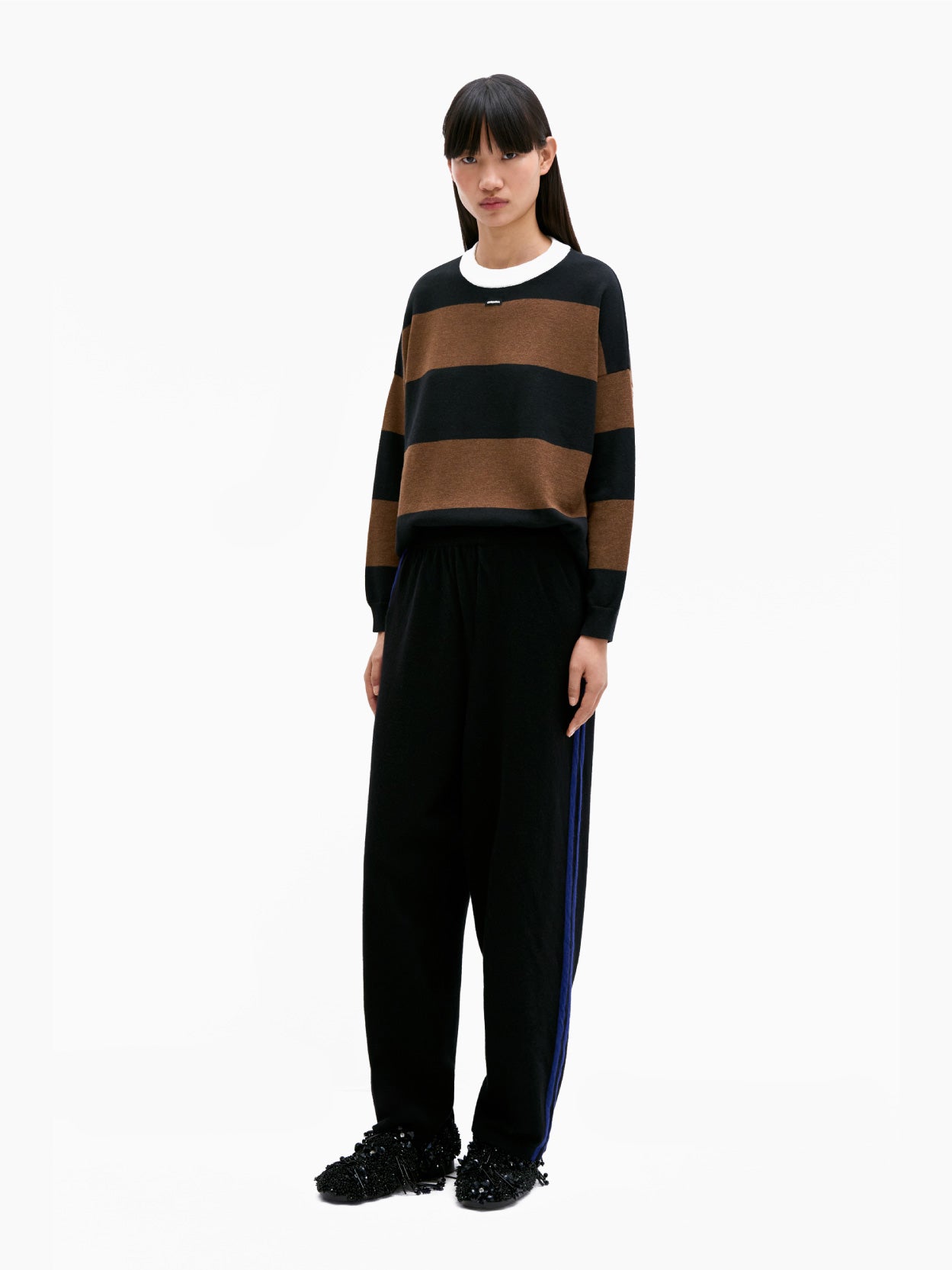 The Cordera Merino Wool Pants in black showcase a simple design with blue side stripes running down the length of each leg. Crafted from premium merino wool and featuring an elasticated waistband, these pants exhibit a relaxed sporty style. They are elegantly displayed on a flat white background.