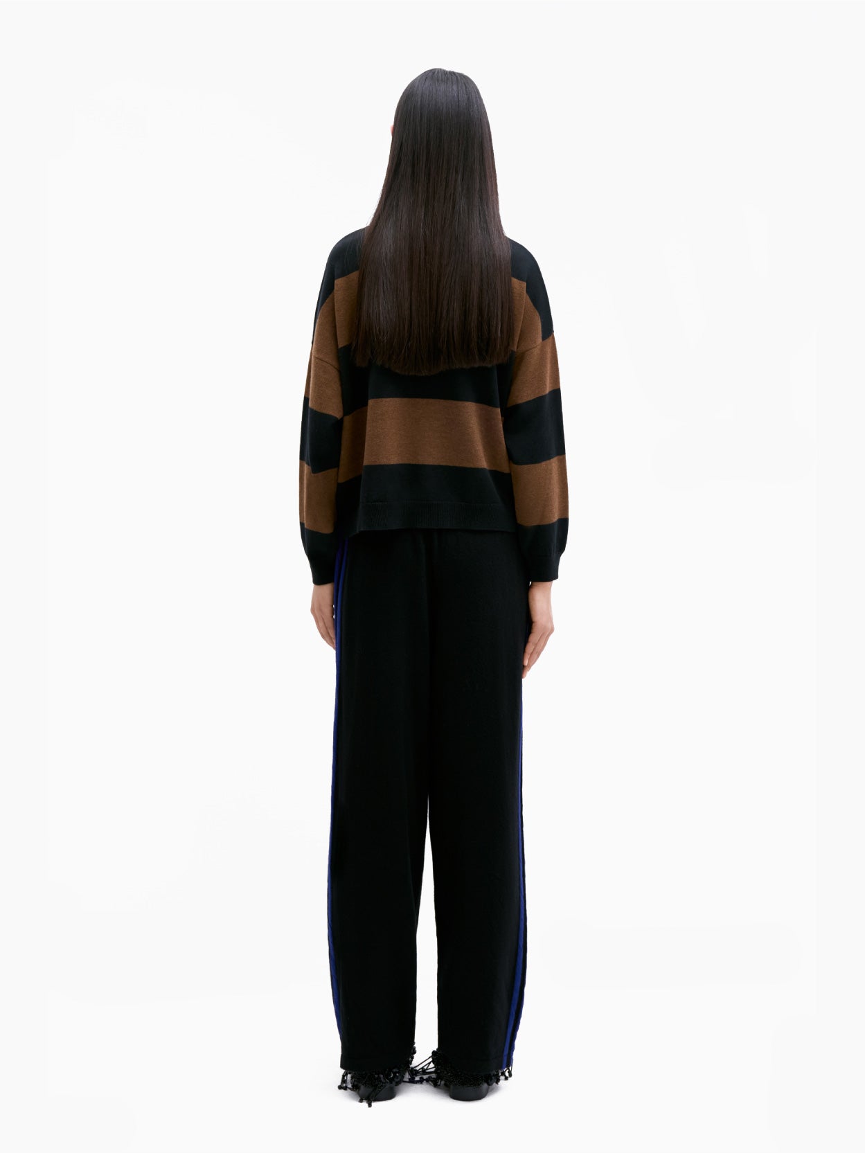 The Cordera Merino Wool Pants in black showcase a simple design with blue side stripes running down the length of each leg. Crafted from premium merino wool and featuring an elasticated waistband, these pants exhibit a relaxed sporty style. They are elegantly displayed on a flat white background.