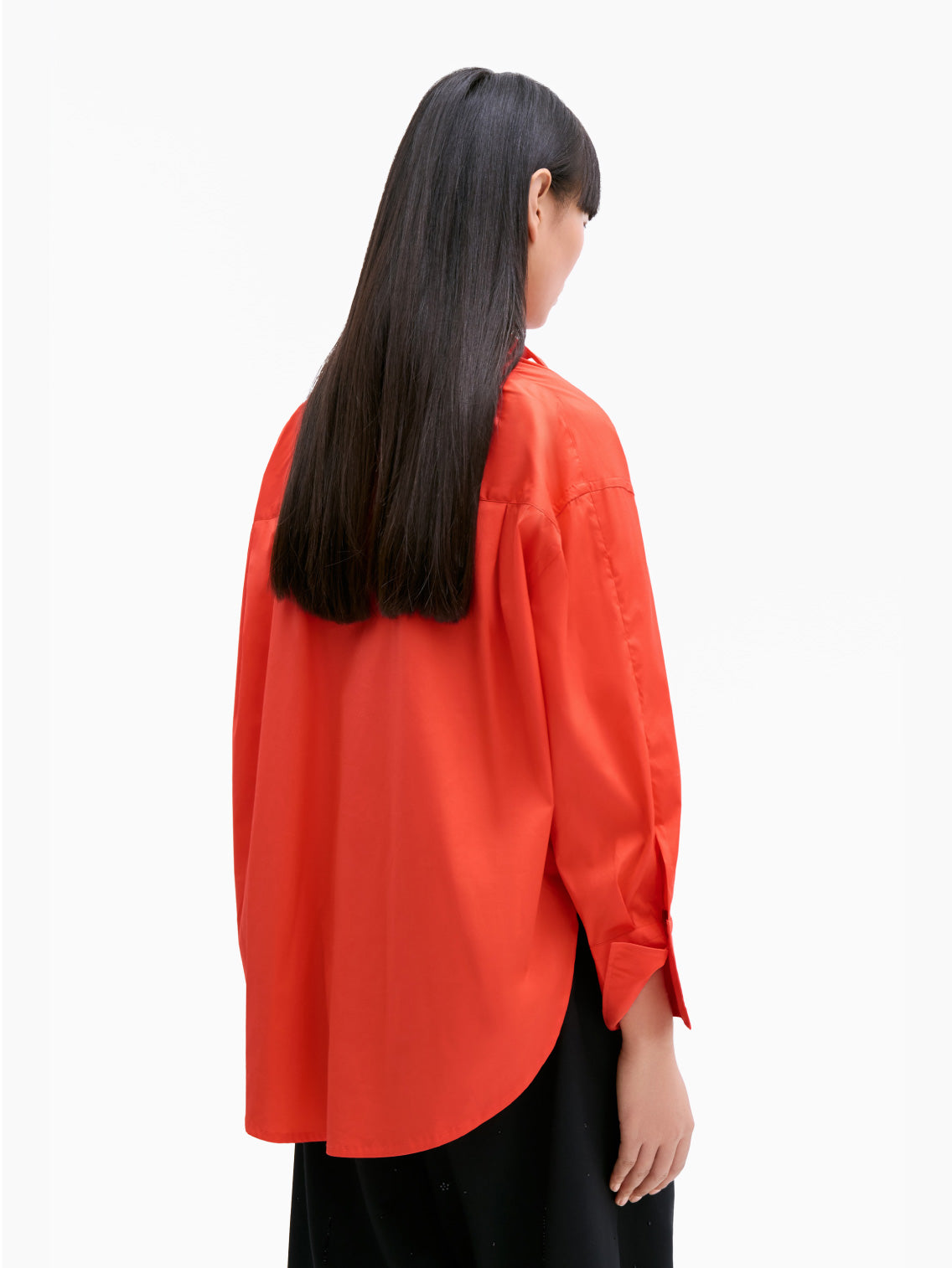 The Cordera Oversize Cotton Shirt in coral is a long-sleeved, pure cotton garment. It features a pointed collar and cuffed sleeves with buttons. Crafted from lightweight fabric, it has an oversized silhouette and a curved hemline. The small, white buttons provide a striking contrast against the coral fabric.