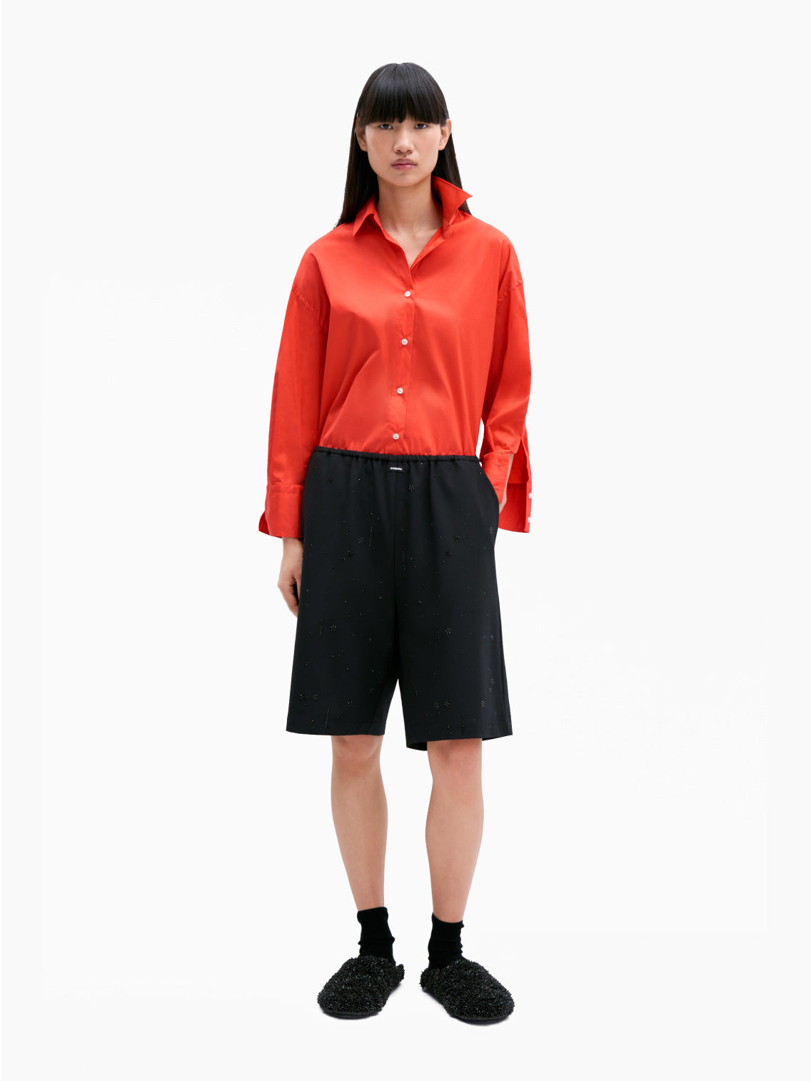 The Cordera Oversize Cotton Shirt in coral is a long-sleeved, pure cotton garment. It features a pointed collar and cuffed sleeves with buttons. Crafted from lightweight fabric, it has an oversized silhouette and a curved hemline. The small, white buttons provide a striking contrast against the coral fabric.