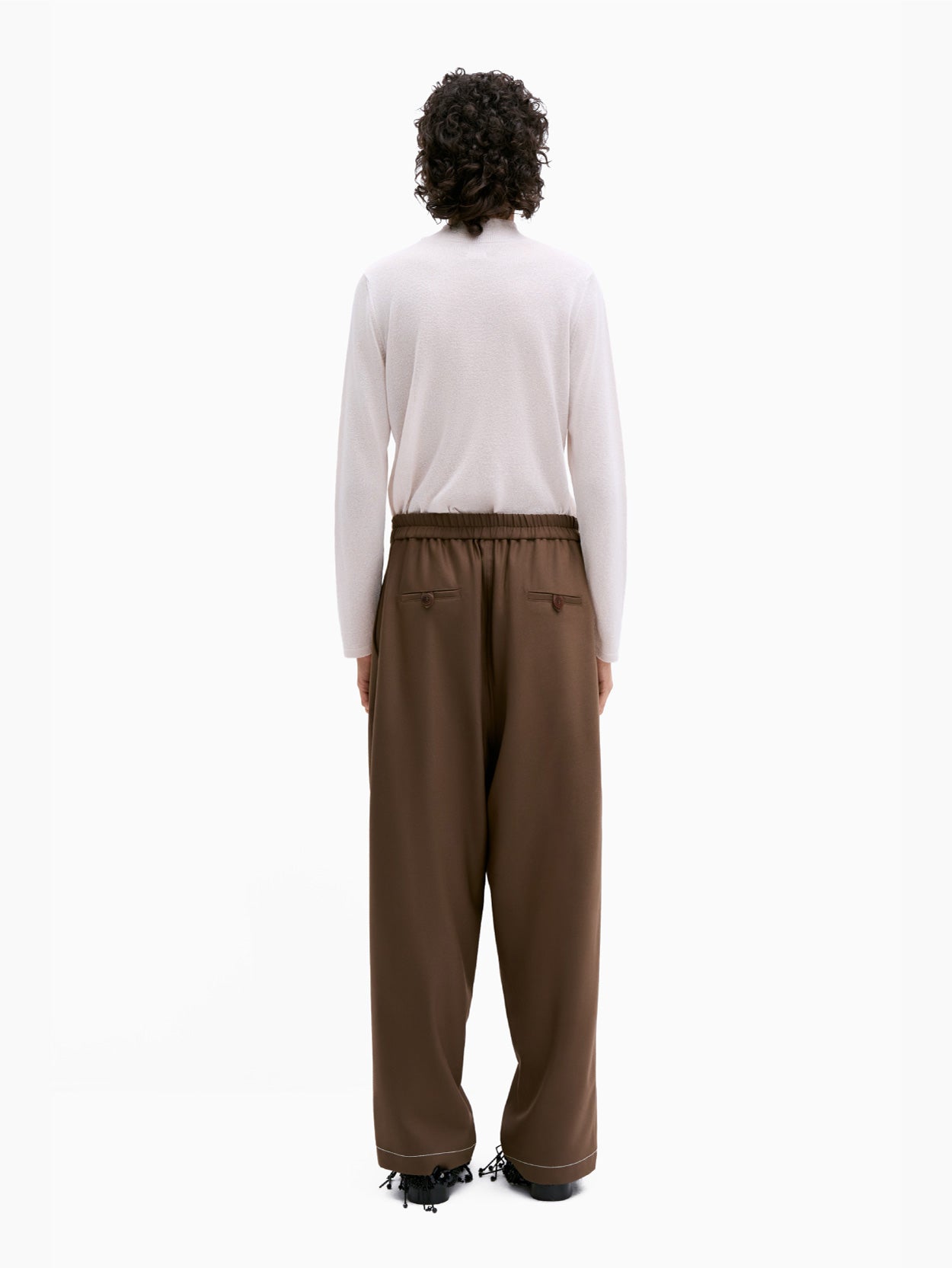 The Tailoring Stitch Pants Otter by Cordera are a pair of dark brown wide-leg pants featuring pleats at the waistband and a button-zipper closure. Crafted from tailored fabric, these cropped ankle pants are wardrobe staples with their smooth texture and contemporary design.