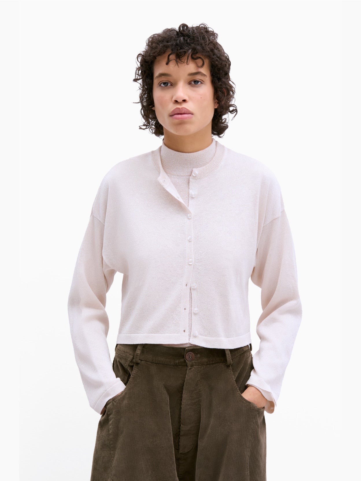 Introducing the Viscose Shimmery Cardigan by Cordera: A light beige, long-sleeved cropped cardigan with a short, boxy fit and a crew neckline. This elegant piece features a button-up front adorned with small, white buttons. Expertly crafted from sustainable viscose, it offers a soft and lightweight fabric. Set against a plain white background.