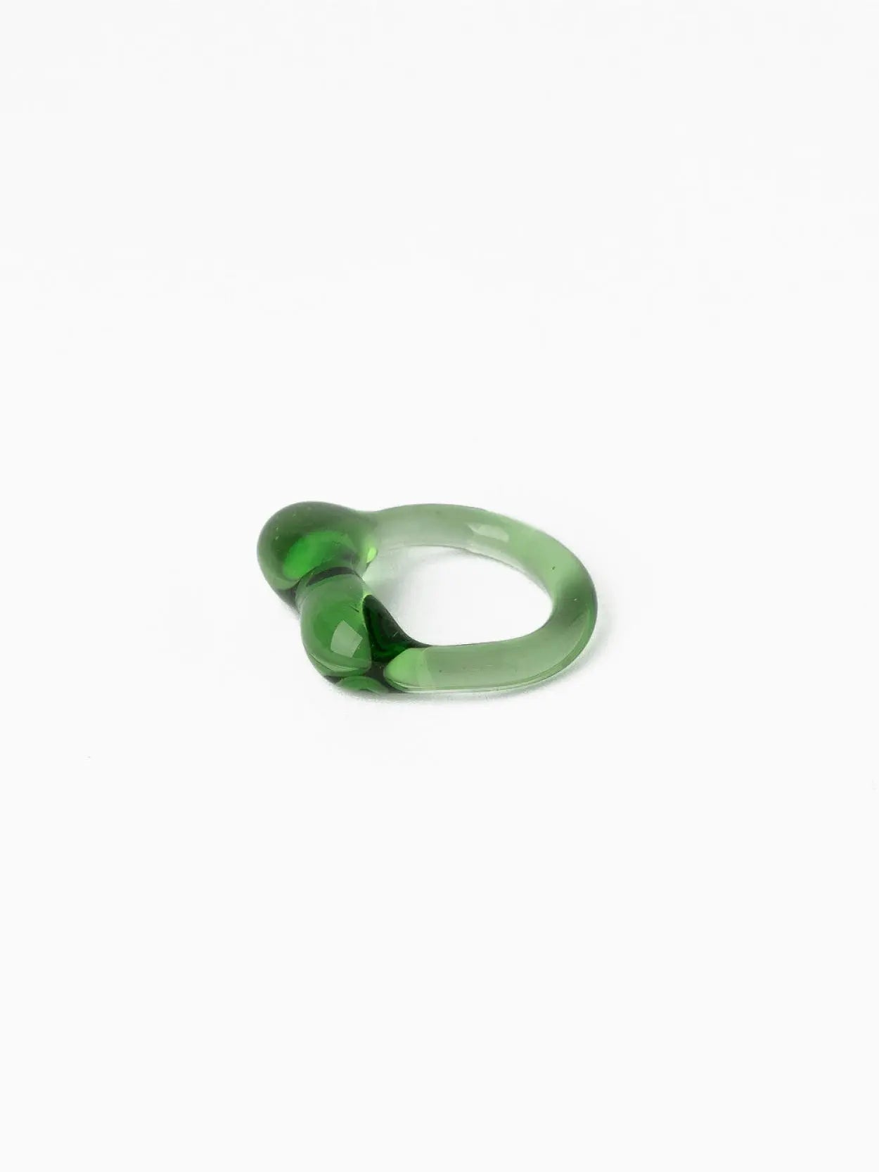 A translucent green ring with organic, bulbous shapes is placed on a plain white background. The design features a smooth finish with a glossy surface, creating a unique and artistic appearance, reminiscent of the avant-garde styles often found in Barcelona's boutique stores. The product is the Caju Ring Green by Nathalie Schreckenberg.