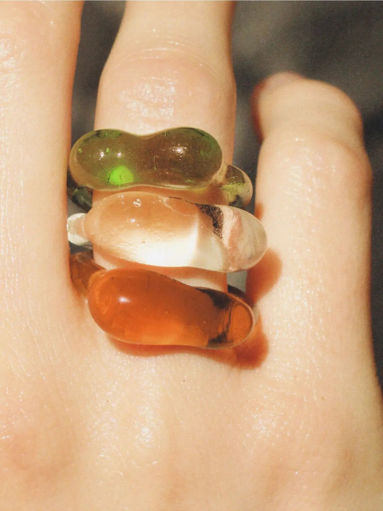 A translucent green ring with organic, bulbous shapes is placed on a plain white background. The design features a smooth finish with a glossy surface, creating a unique and artistic appearance, reminiscent of the avant-garde styles often found in Barcelona's boutique stores. The product is the Caju Ring Green by Nathalie Schreckenberg.