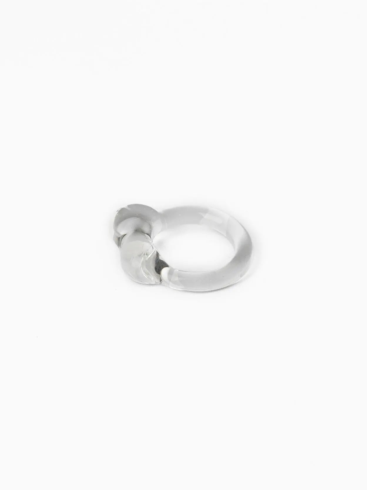 A sleek, modern silver ring with a rounded, abstract design on top, placed on a white background. The ring's minimalist style and smooth finish give it a contemporary and elegant appearance, perfect for showcasing in any Barcelona boutique or Bassalstore display. The Caju Ring Transparent by Nathalie Schreckenberg exemplifies these qualities beautifully.
