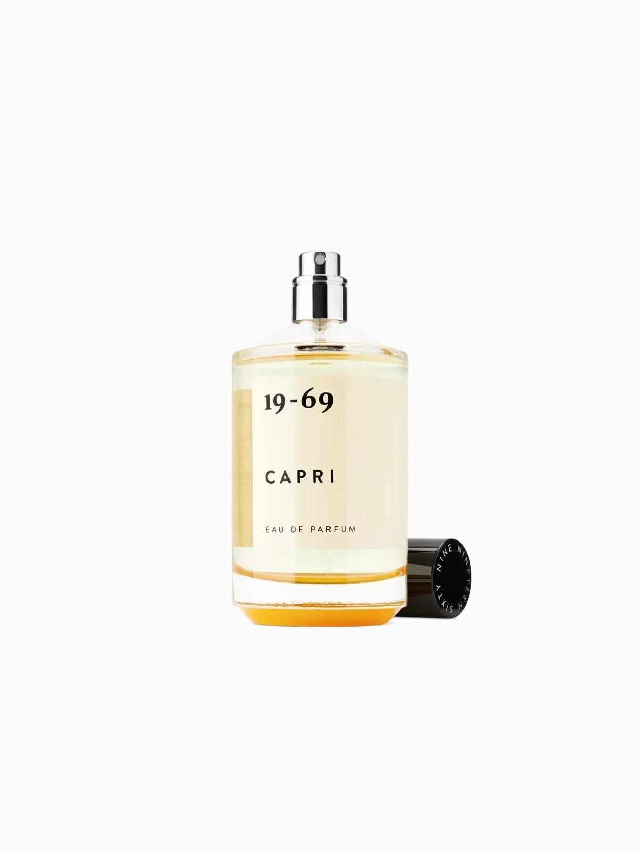 A clear glass bottle of Capri 100ml by 19-69 with a black cap, available at Bassalstore. The fragrance name "Capri 100ml" and "19-69" text is printed on the front in black, showcasing a yellow-tinted liquid inside.
