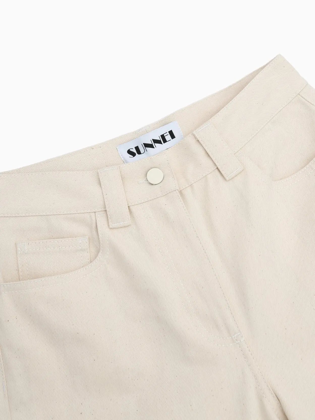 A pair of cream-colored straight-leg jeans with large, wide cuffs at the bottom. The cuffs feature vertical beige and white stripes. The Classic Denim Pants White Stripes by Sunnei, available at Bassalstore in Barcelona, have a classic five-pocket design with a button and zipper closure against a plain white background.