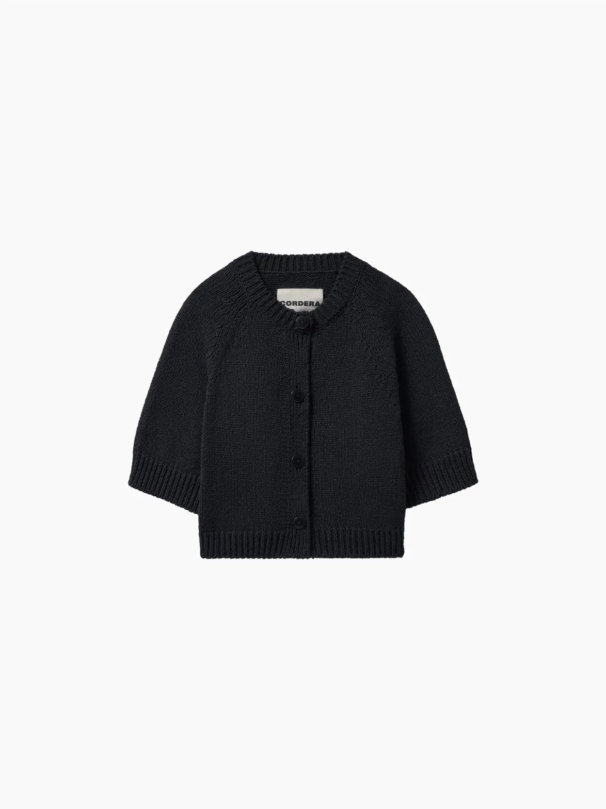 A black, long-sleeved baby cardigan with a crew neck and button-up front. The Cotton Buttoned Top Black, made of knitted fabric, is displayed on a plain white background. The label inside reads "Cordera." Available exclusively at bassalstore in Barcelona.