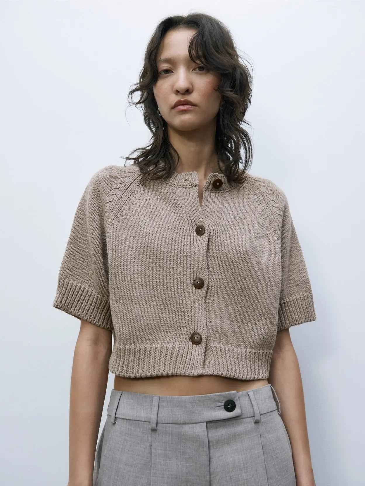 A beige knit **Cotton Buttoned Top Taupe** with long sleeves, a round neckline, and three brown buttons down the front. The top has a ribbed hem and cuffs, and a white label inside with text. Displayed against a plain white background, it’s available exclusively at Bassalstore in Barcelona by **Cordera**.
