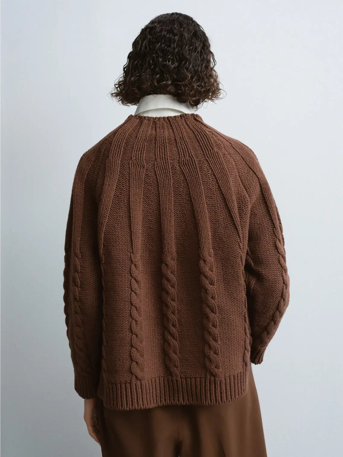 Cotton Cable Sweater Madera with a crew neck by Cordera. The sweater features intricate braided patterns on the front and sleeves, and ribbing at the collar, cuffs, and hem. The overall design is cozy and suitable for cool weather. Find this timeless piece at our Barcelona-based Bassalstore.