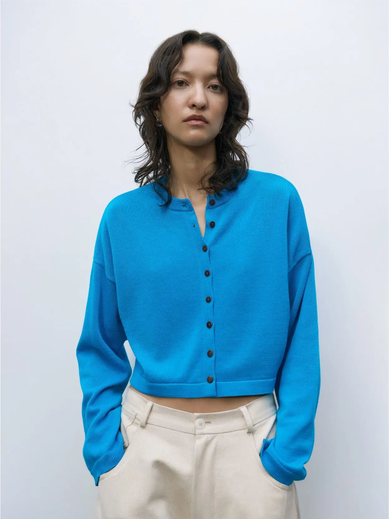 A bright blue, long-sleeve Cotton Cropped Cardigan Ceruleo with a round neckline and black buttons down the front, available exclusively at Bassalstore in Barcelona. The cardigan is displayed against a white background.