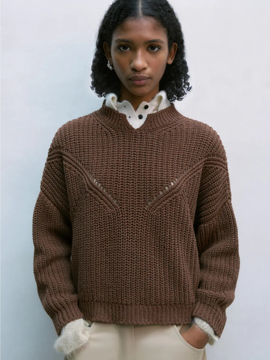A brown knitted sweater with a round neckline and a relaxed fit. The Cotton Cropped Sweater Madera, available at Bassalstore in Barcelona, features a geometric knit pattern with triangular openwork details on the front and ribbed cuffs, hem, and neckline. The texture appears thick and cozy, ideal for cooler weather. This exquisite piece is from the brand Cordera.