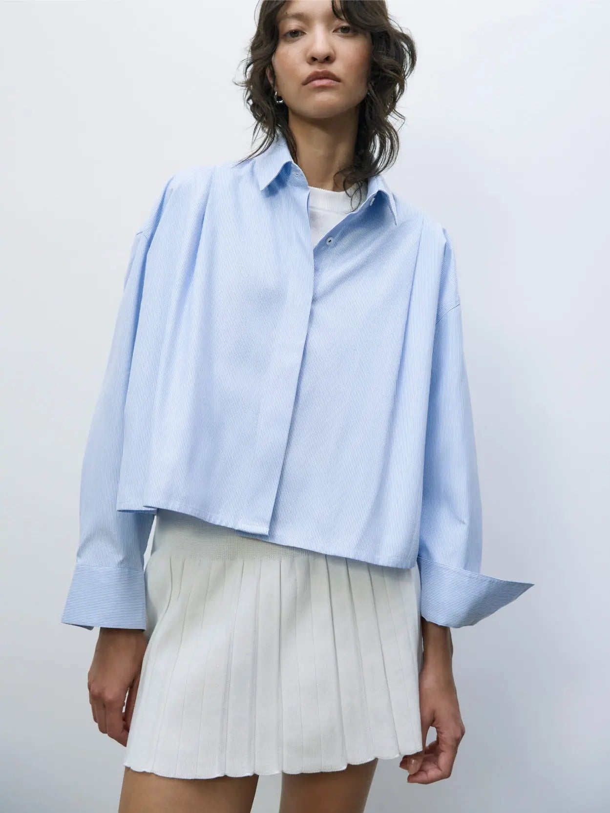 A Cotton Pleated Skirt White by Cordera, showcased against a plain light gray background, features a fitted waistband and multiple sharp pleats creating a structured and stylish look. Find this chic piece at Bassalstore in Barcelona.