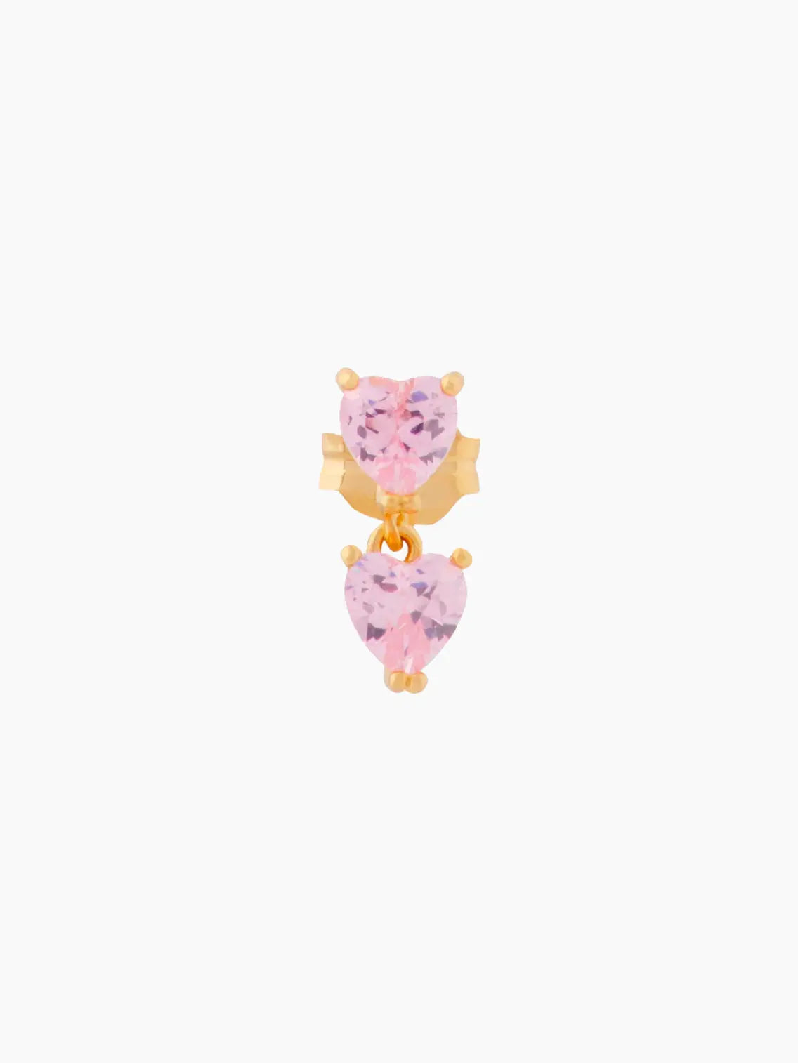 A Double Whisper Heart Stud Pink from Wilhelmina Garcia in Barcelona, featuring two pink heart-shaped gemstones. One gemstone is fixed at the top while another dangles below it, both set in gold clasps. The design is simple and elegant, with a focus on the pink gemstones.