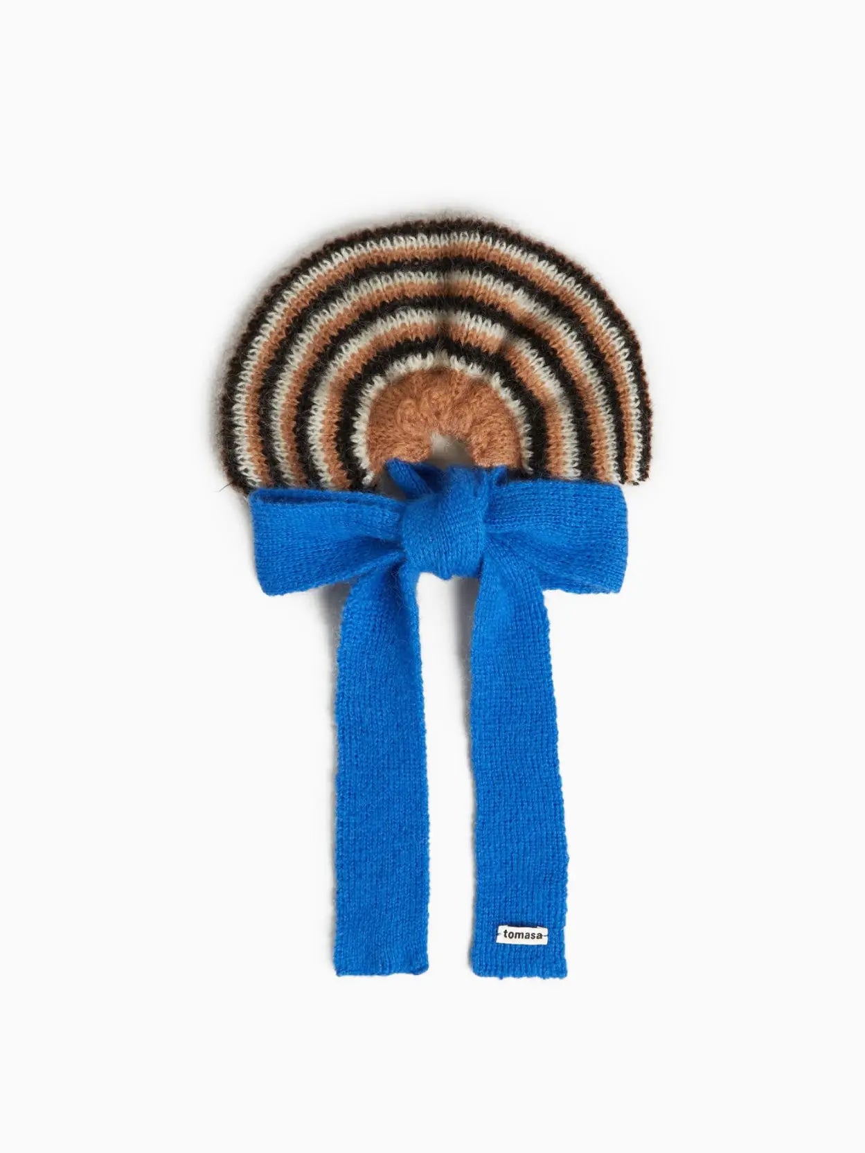 A Eugenia Bow Scrunchie designed with brown, cream, and black stripes in a circular pattern. Attached is a bright blue knitted scarf tied in a front knot, featuring a small white label with the brand name "Tomasa." Available exclusively at Bassalstore in Barcelona, the scrunchie and scarf appear as a single accessory.