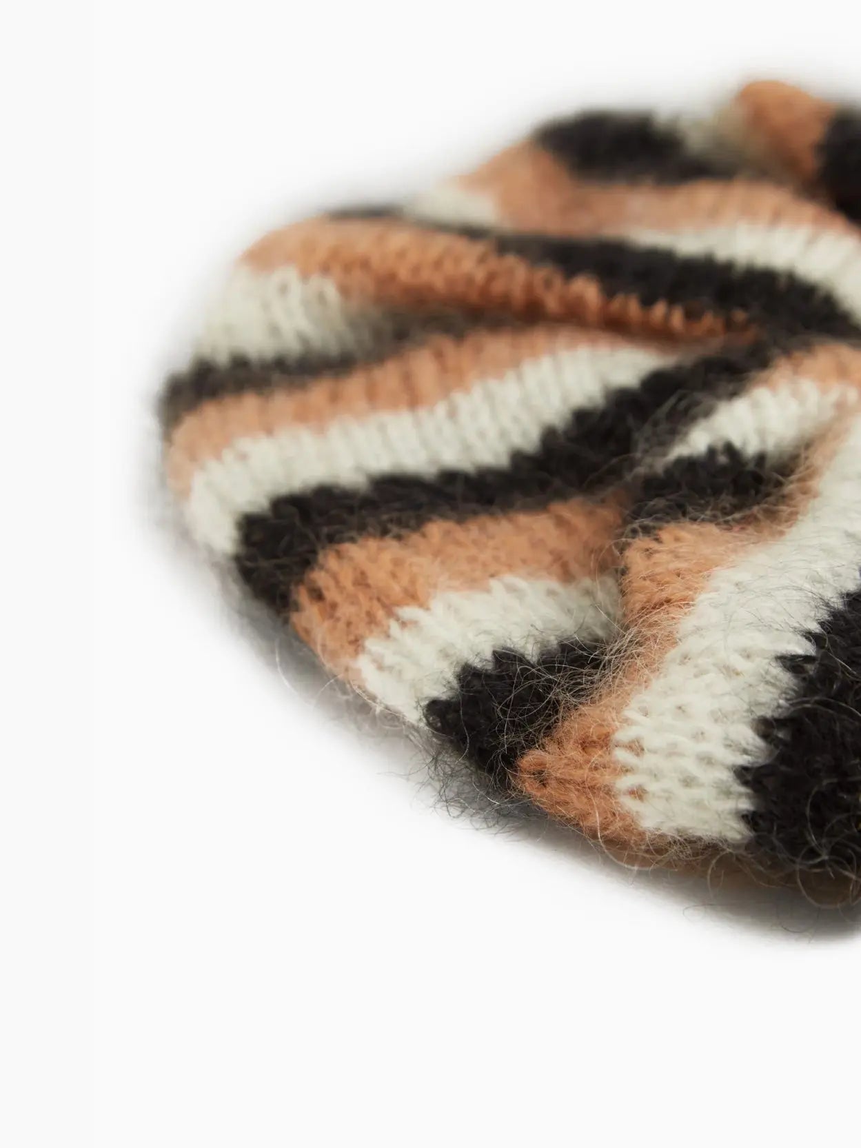 A fuzzy round Tomasa Eugenia Scrunchie with alternating stripes of cream, brown, and black is available at Bassalstore. The scrunchie has a soft texture and a tightly gathered center.