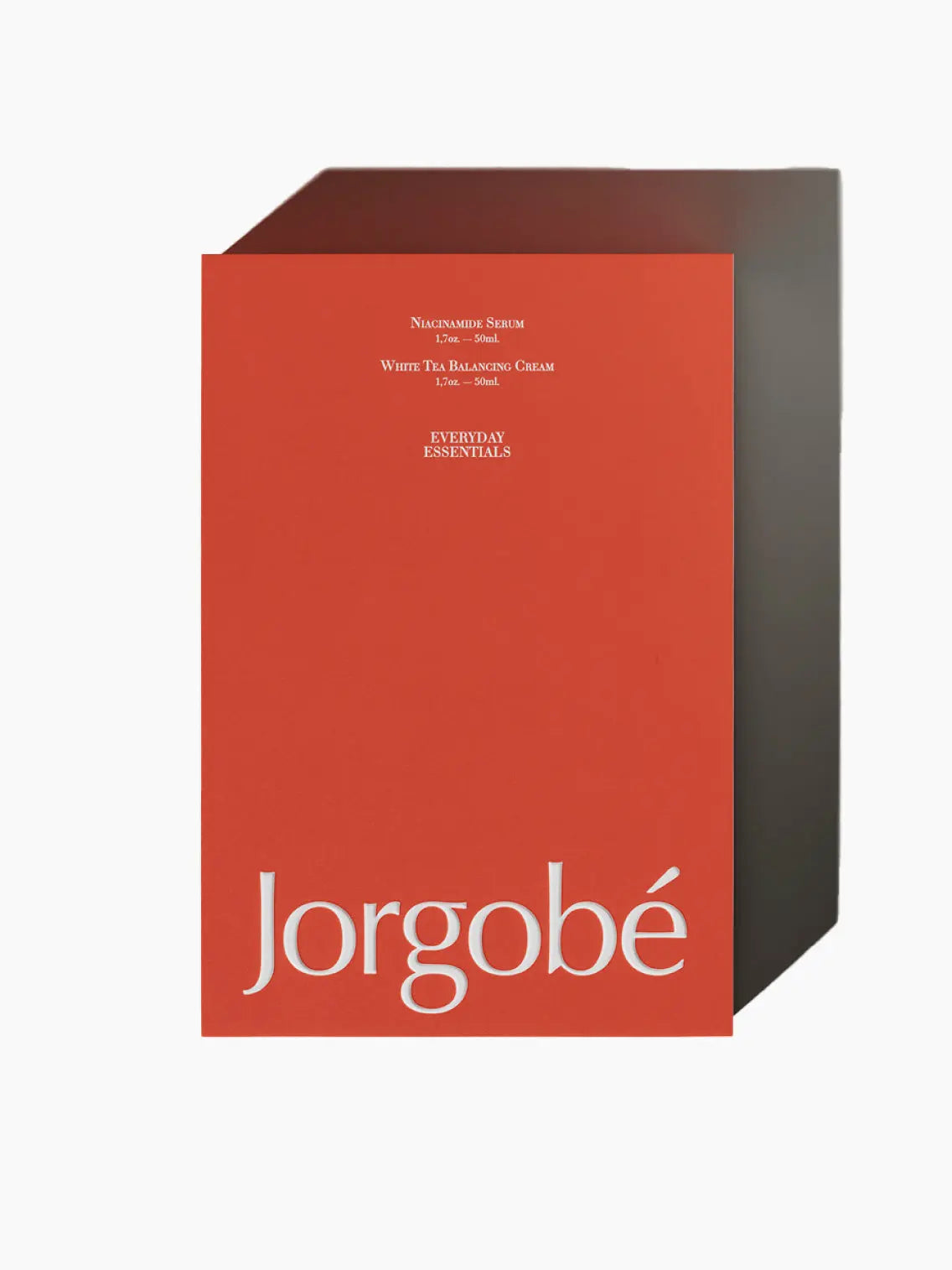 A red rectangular product packaging with the brand name "Jorgobé" in large white letters at the bottom. The text mentions the product contents: niacinamide serum, hand scrub, and white tea balancing cream. The phrase "Everyday Essentials Red Sleeve" is also included. Available exclusively at Bassal Store in Barcelona.