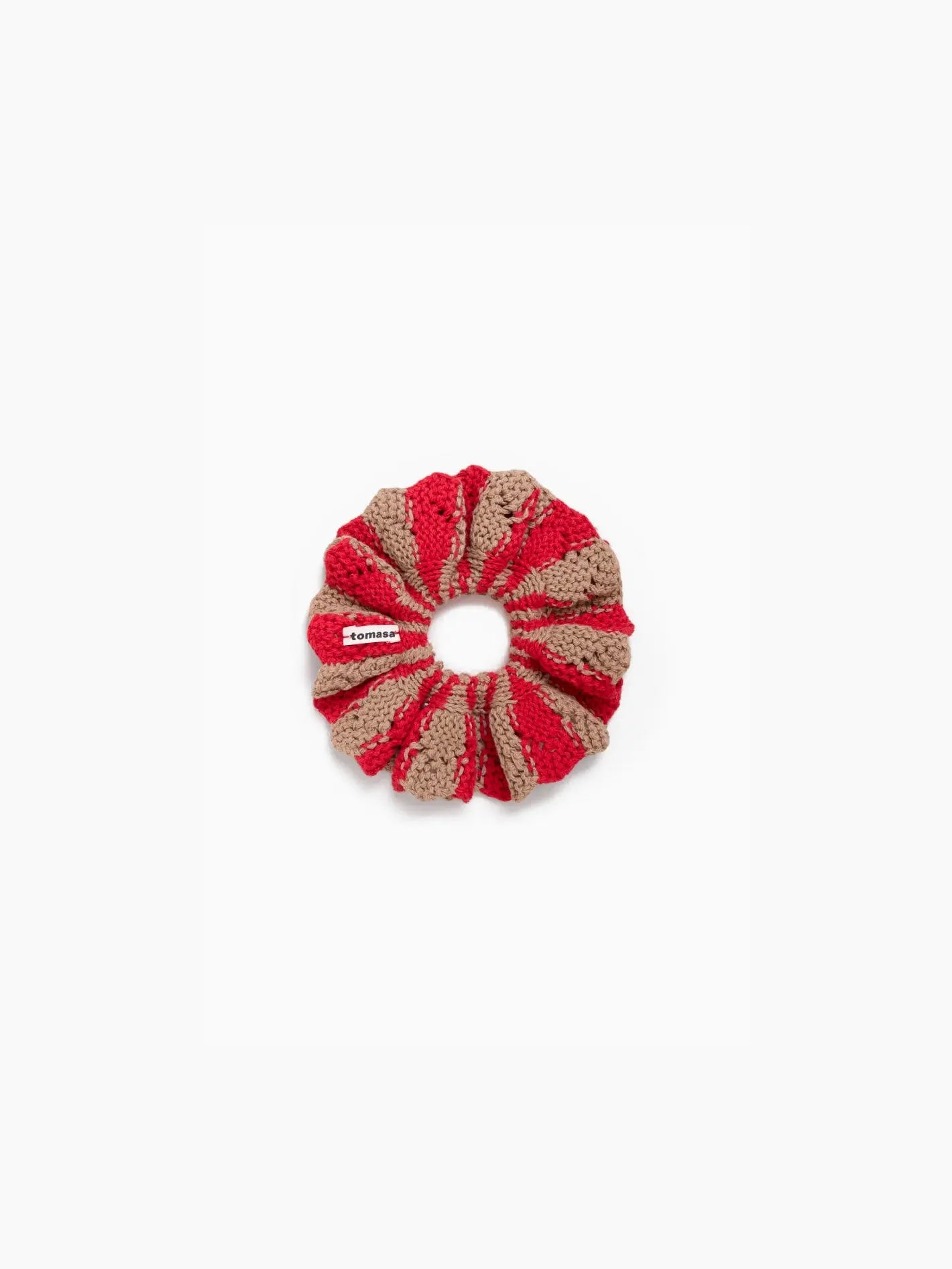 A Fernandita Scrunchie Amapola made of red and beige yarn with a textured pattern. It has a small rectangular white tag attached with red text. Displayed against a plain white background, this elegant accessory by Tomasa is available exclusively at Bassalstore in Barcelona.