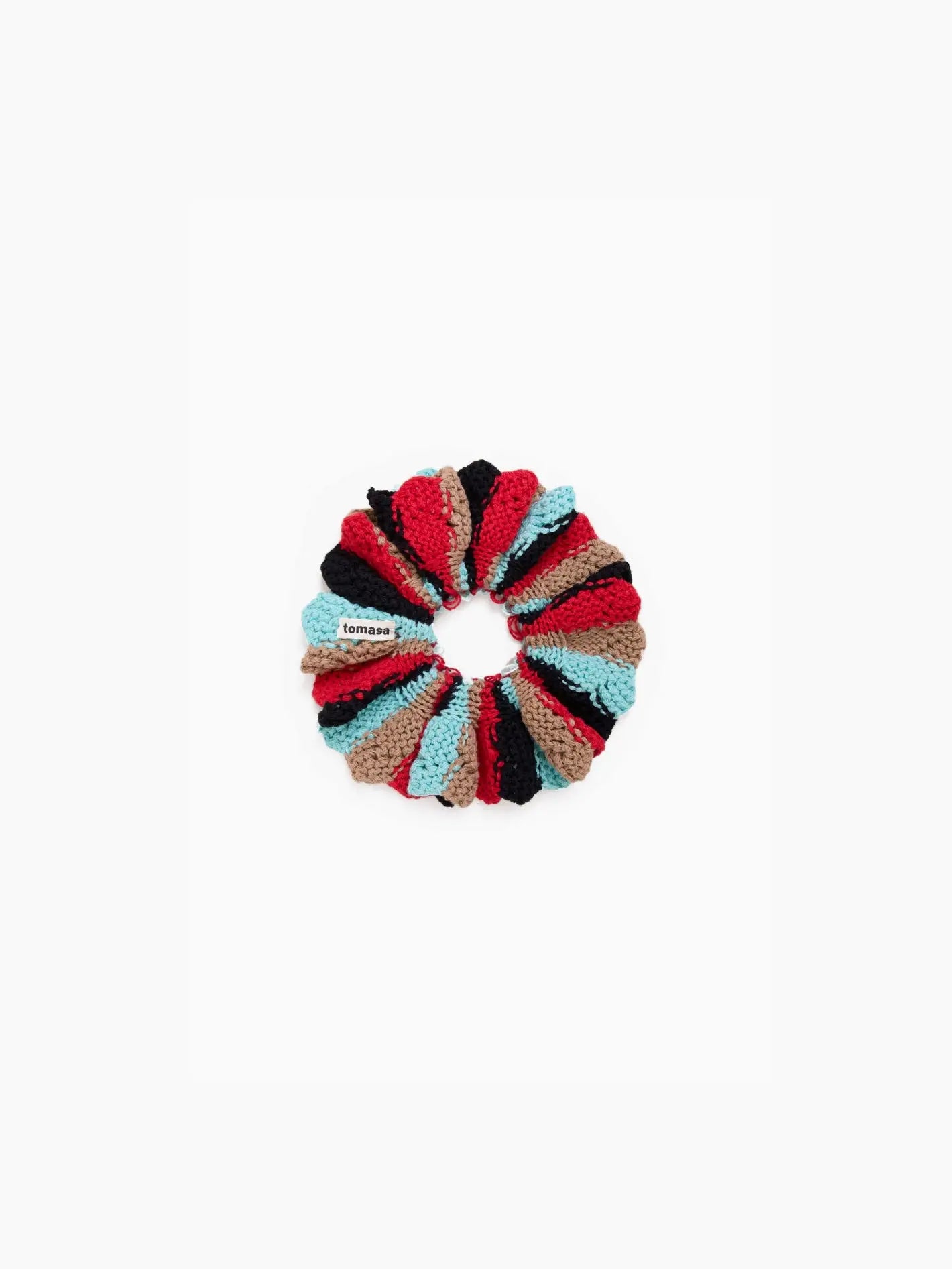 A multicolored, crocheted Fernandita Scrunchie Berber made up of alternating segments in red, black, blue, and beige. It is circular and has a visible fabric brand tag labeled "Tomasa." Available at bassalstore in Barcelona. The background is plain white.