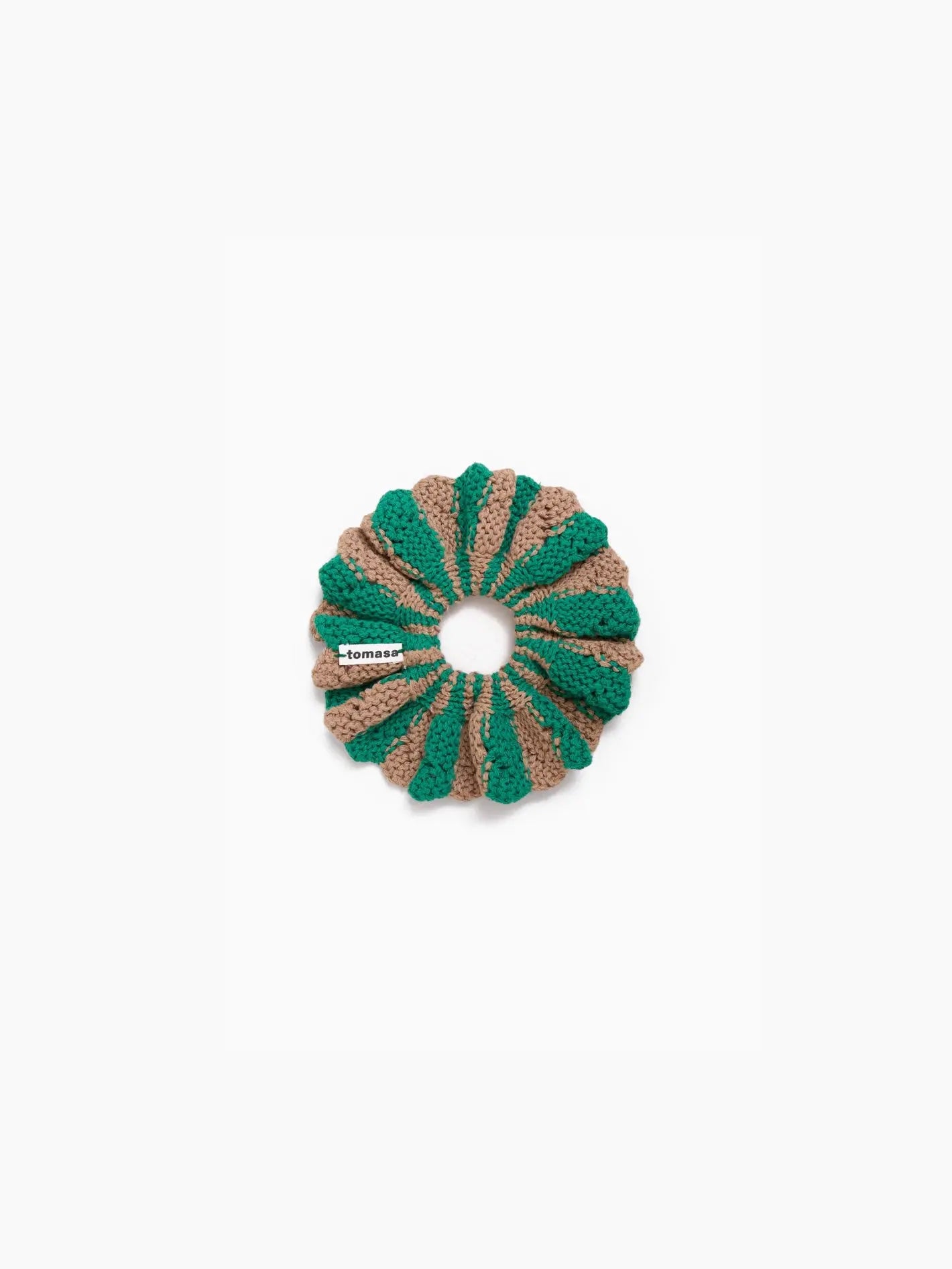 A round, textured hair scrunchie with alternating green and beige sections, displayed on a plain white background. A small tag with the brand name "Tomasa" is attached to the scrunchie. Available exclusively at Bassalstore in Barcelona.