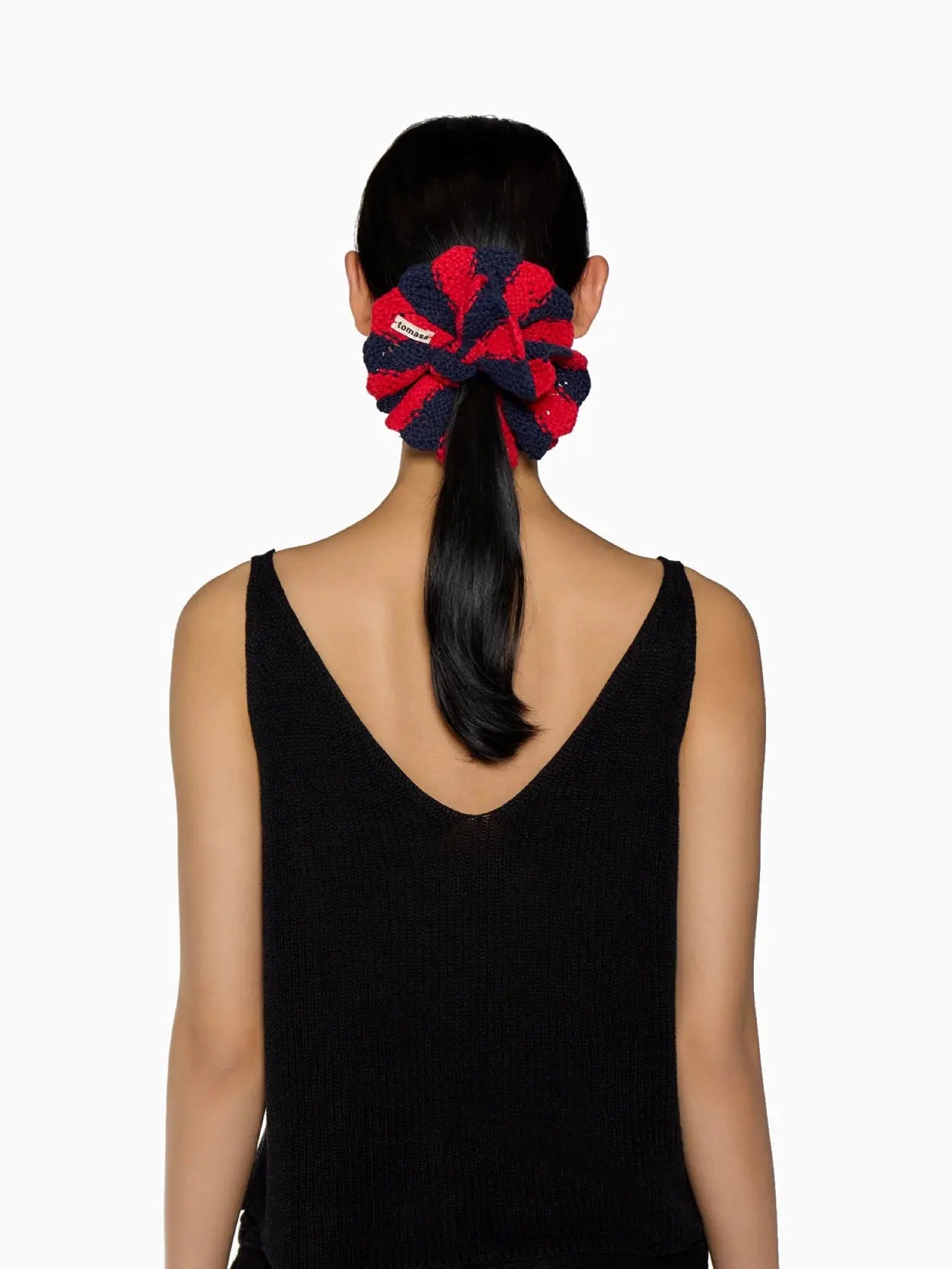 A circular hair scrunchie made of knitted fabric with alternating red and dark blue stripes, featuring a small white and red tag labeled "Tomasa." Perfect for any fashion enthusiast, this stylish accessory is now available at bassalstore in Barcelona. The background is plain white.